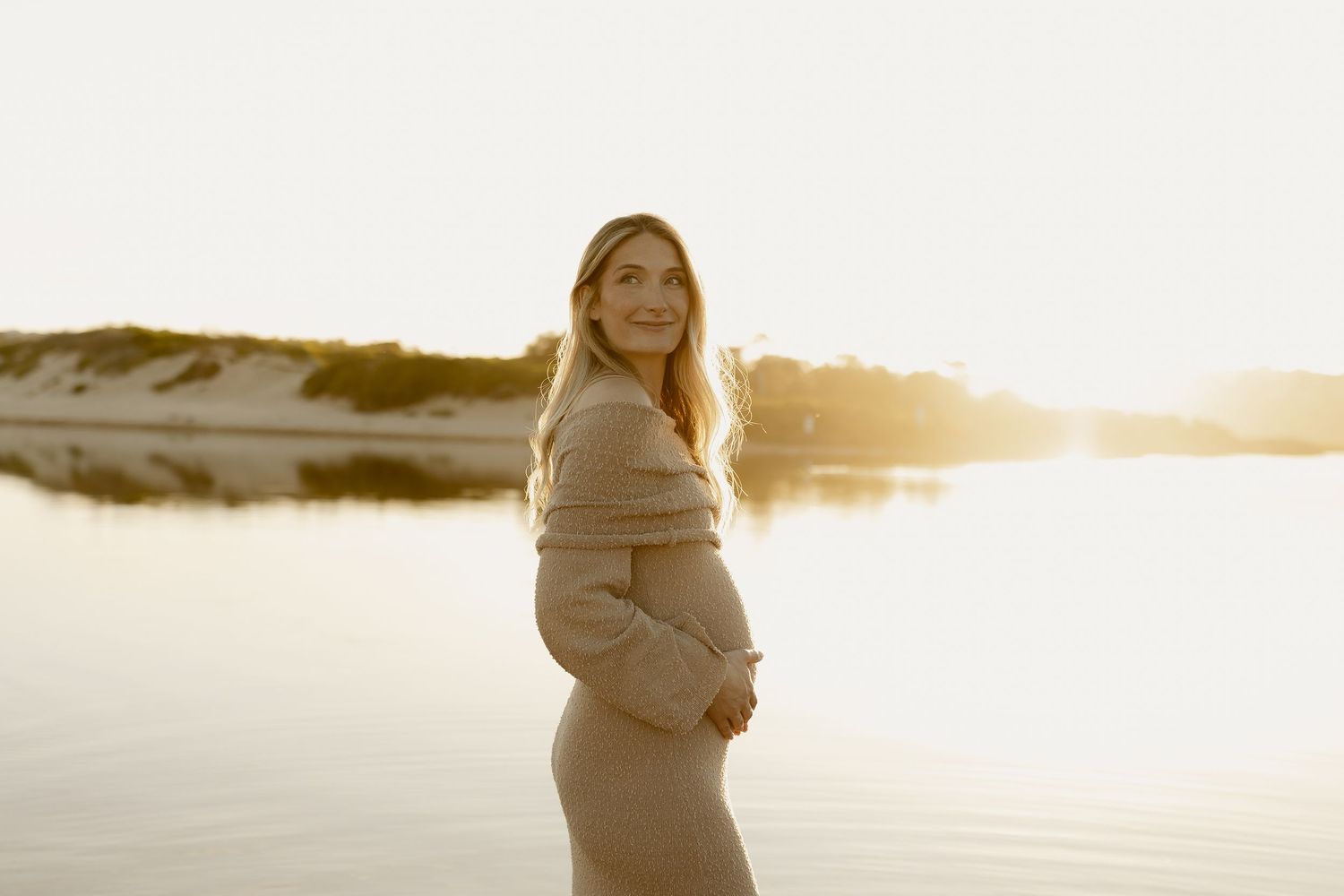 Ethereal portrait of someone in a flowing white dress against a golden sunset by a serene lake.