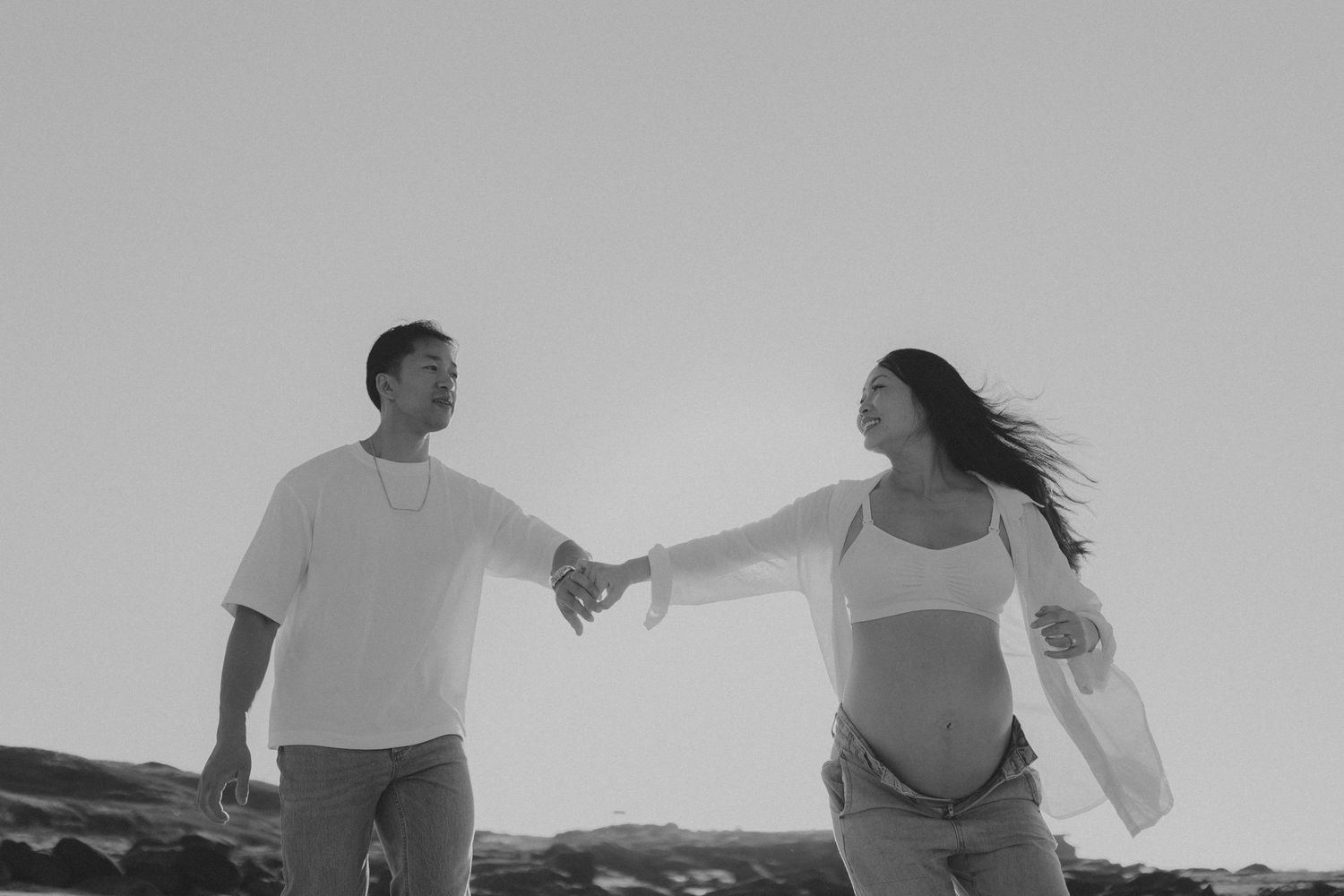Black and white photo of two people walking hand in hand on a scenic cliff overlook.
