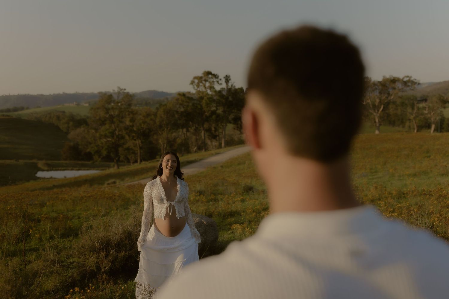 Couple embraces on grassy hillside during romantic sunset photoshoot.