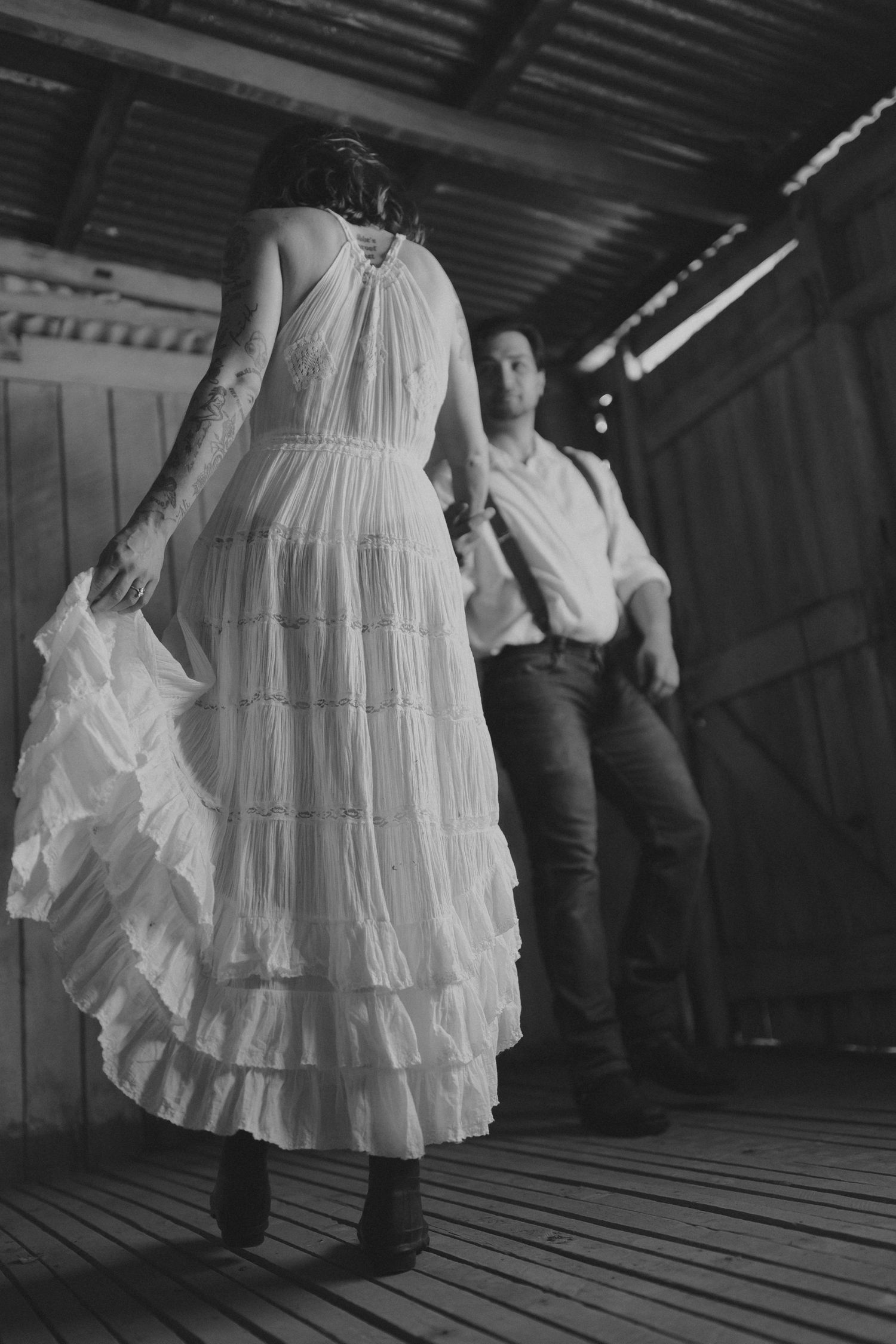 A black and white photo captures movement of a white ruffled dress in a wooden barn setting.