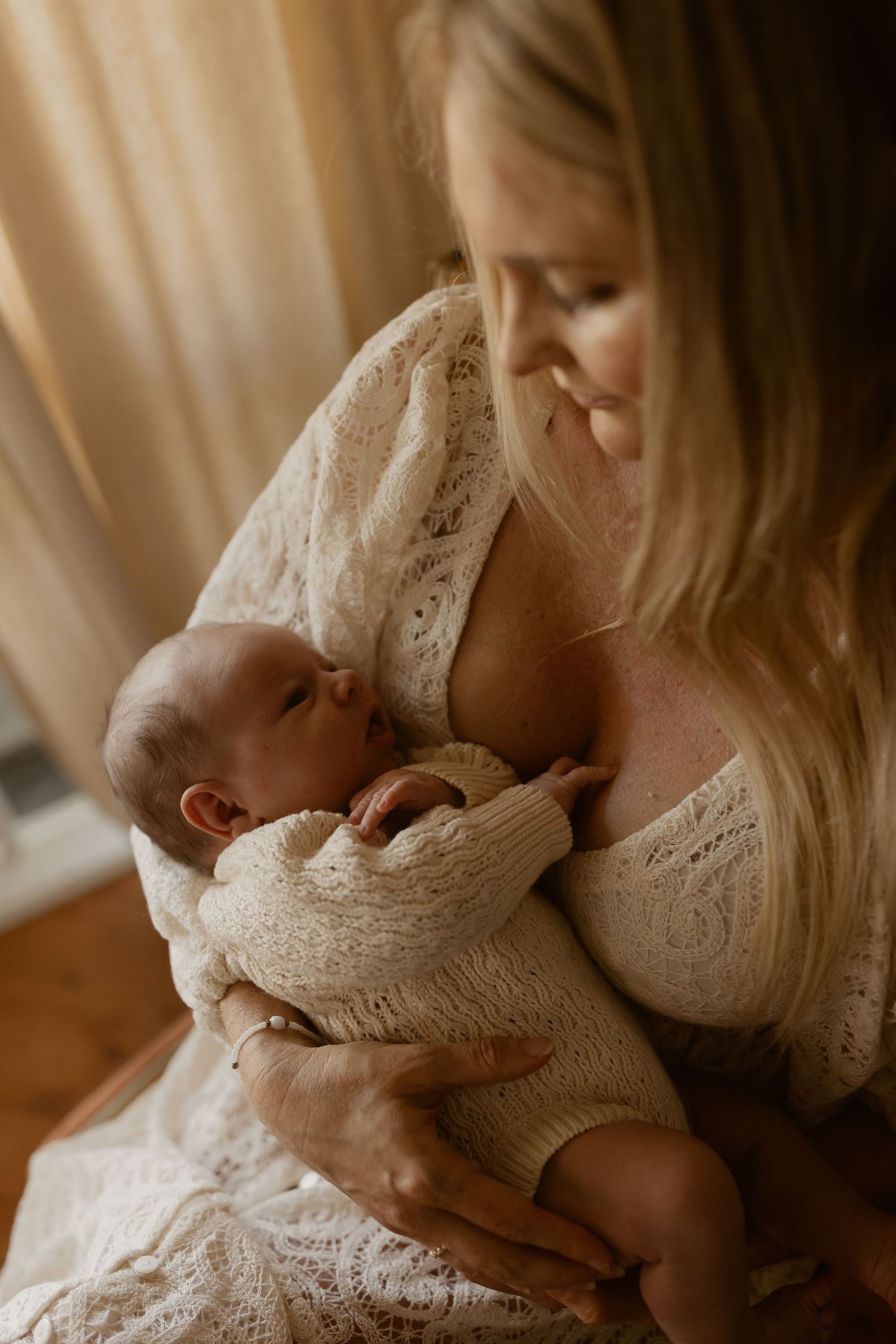 A tender moment between mother and newborn baby wearing knitted cream outfits in warm natural lighting.