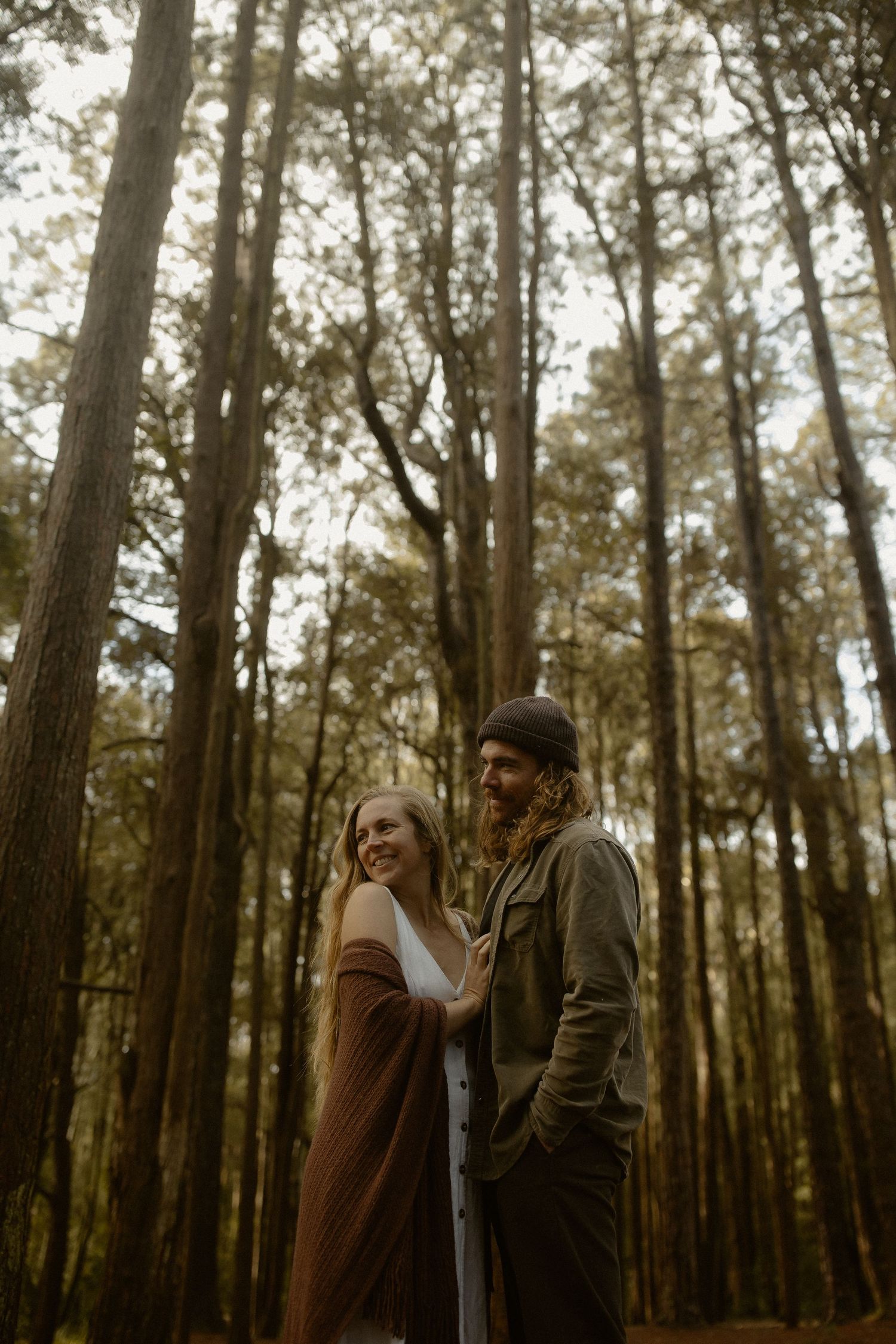 Romantic couple embraces in a misty forest setting wearing casual autumn clothing.