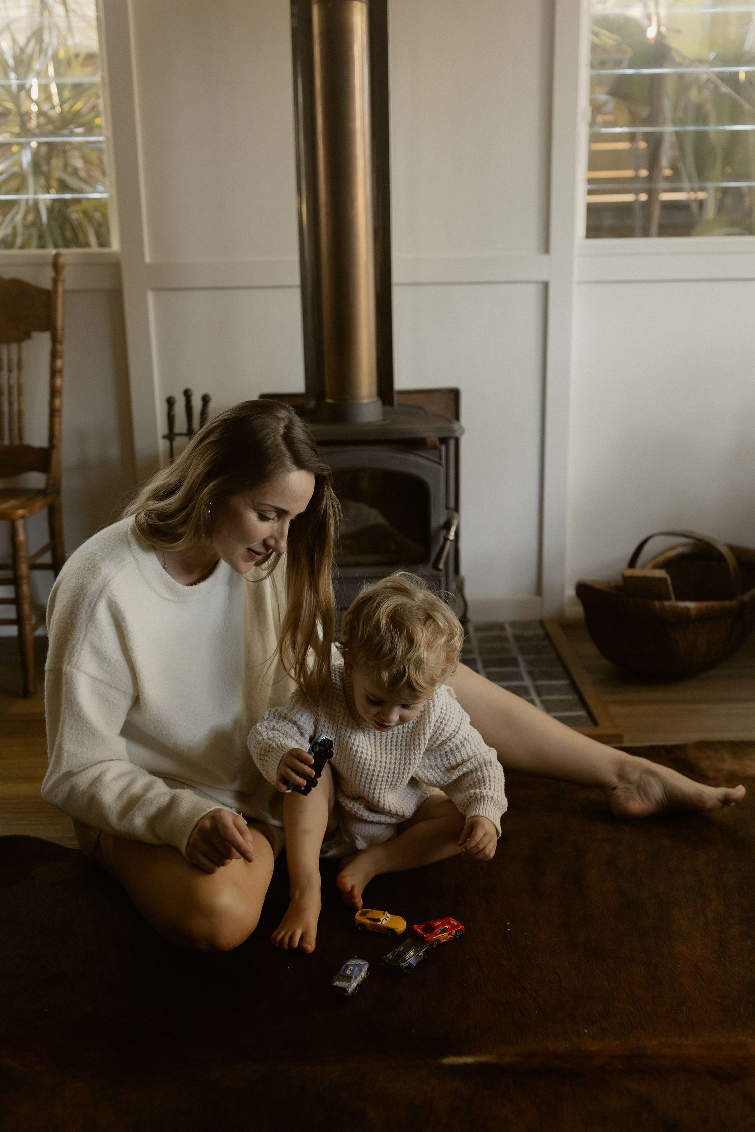 Parent and child playing with toys together on wooden floor near wood burning stove.