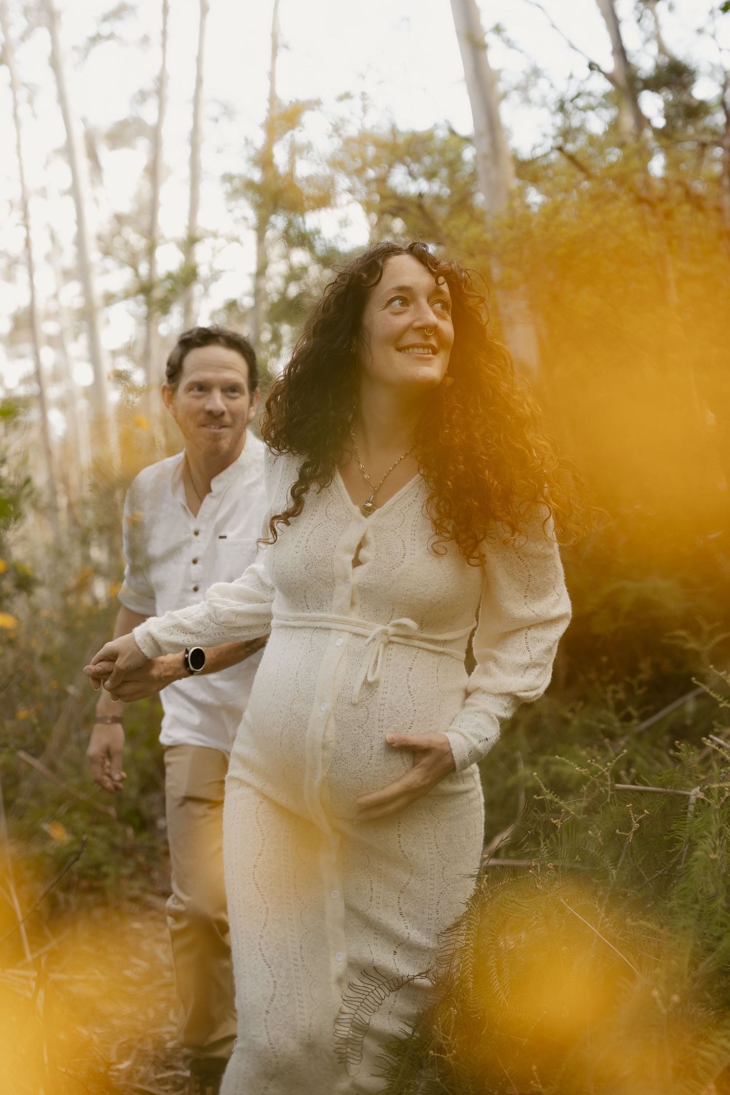 A couple shares a tender moment in nature with golden sunlight filtering through the trees.