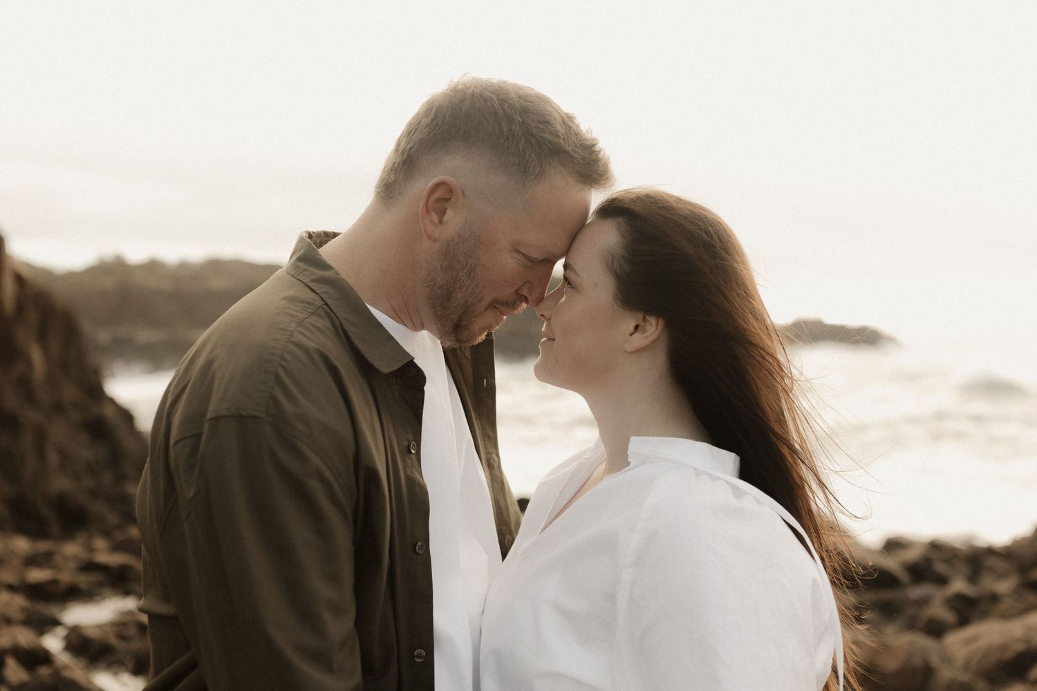 Romantic couple embraces against scenic coastal backdrop during golden hour sunset.