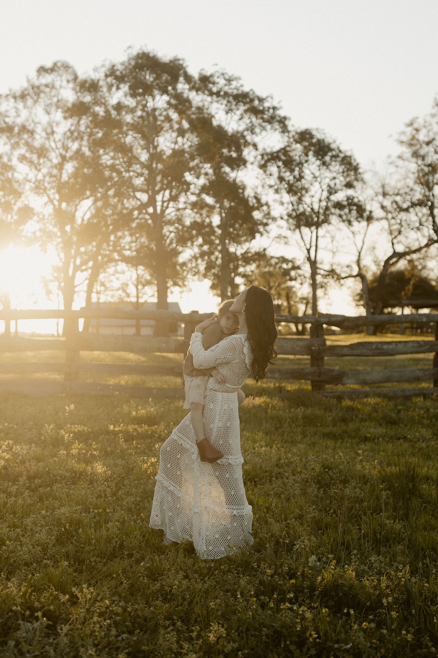 A figure in a flowing white dress dances gracefully in a sunlit meadow during golden hour.