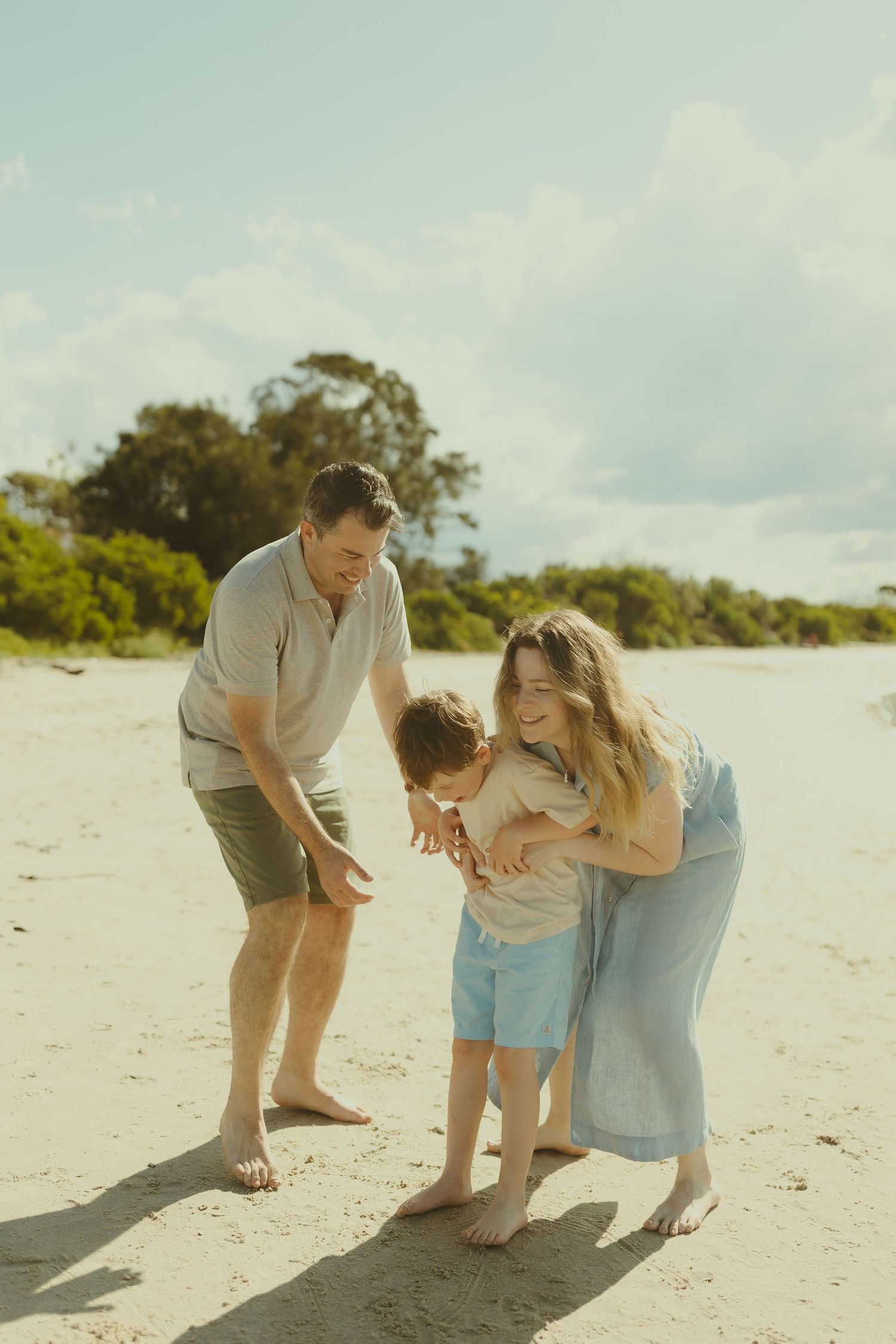 Playful family moment captured on a bright sandy beach with laughter and joy.