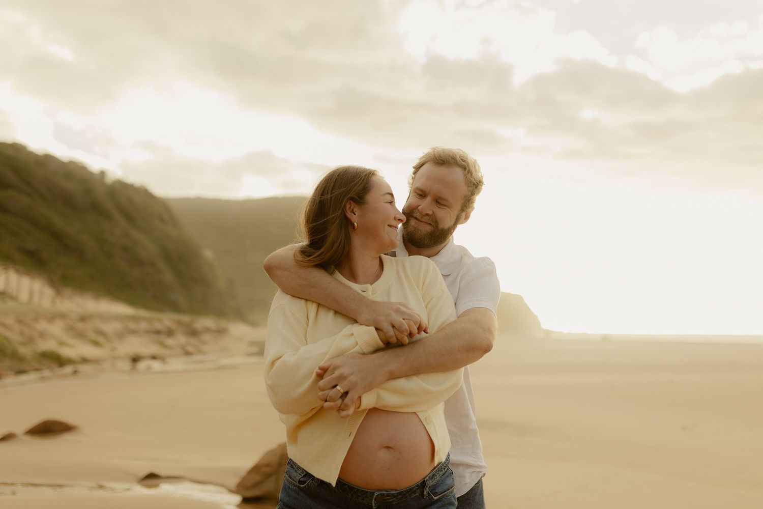 Romantic couple shares tender moment on sandy beach during golden hour.