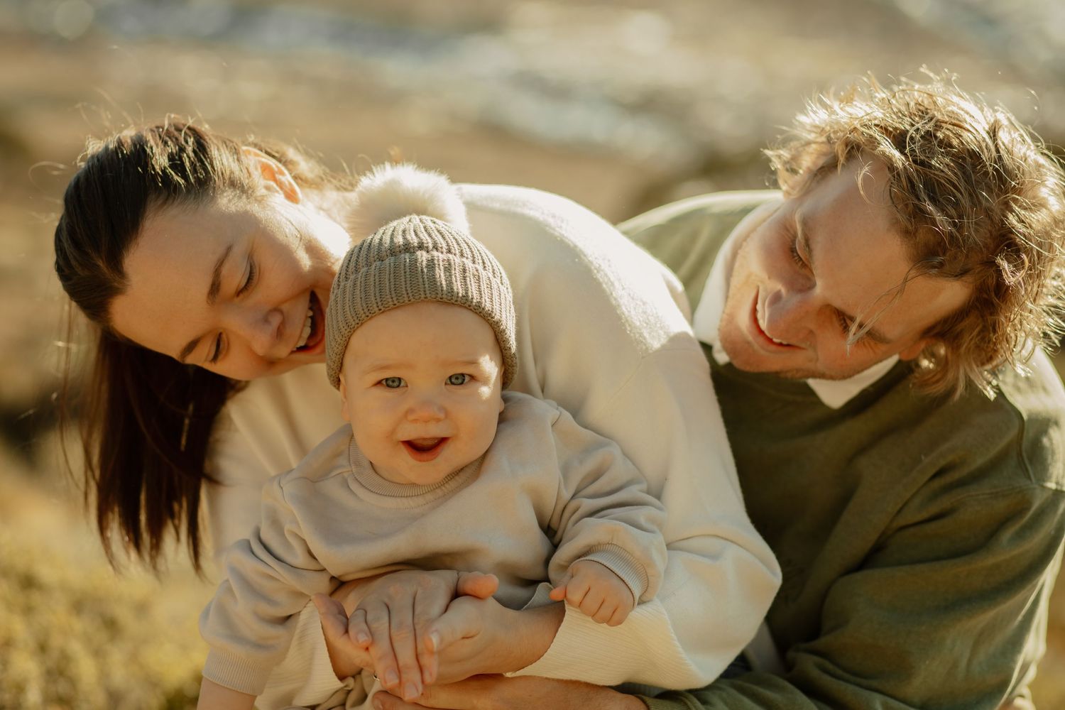 Family cuddles together outdoors against scenic mountain backdrop in warm sunset light.