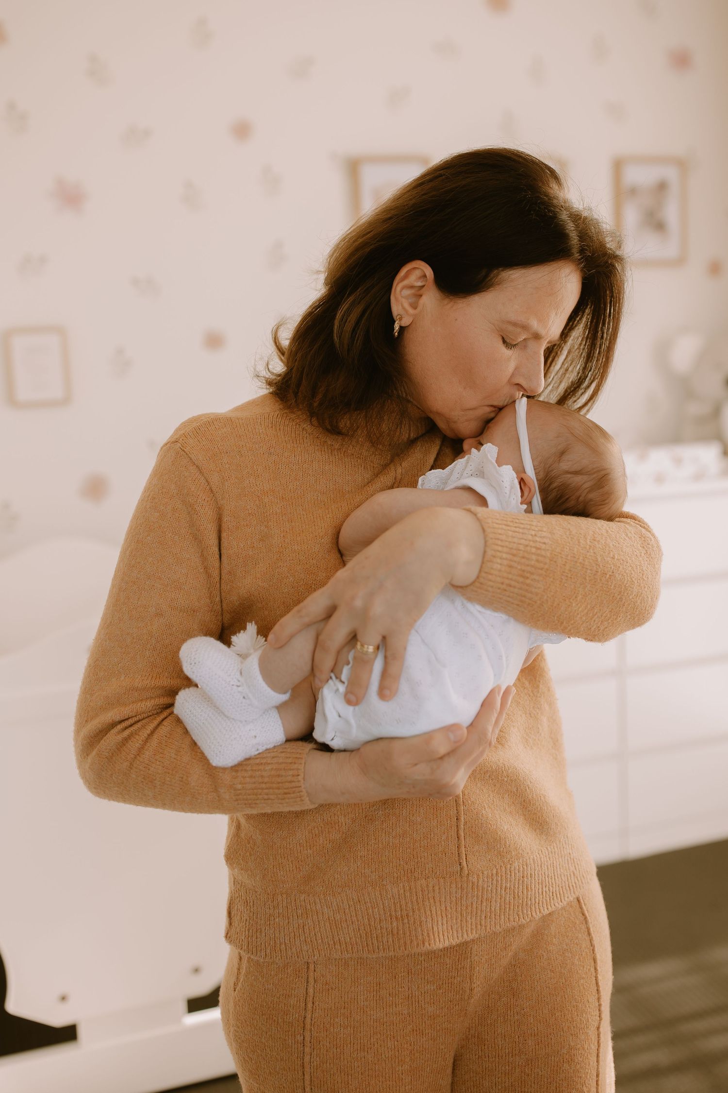 A person in a tan sweater tenderly cradling and gazing at a newborn baby swaddled in white.