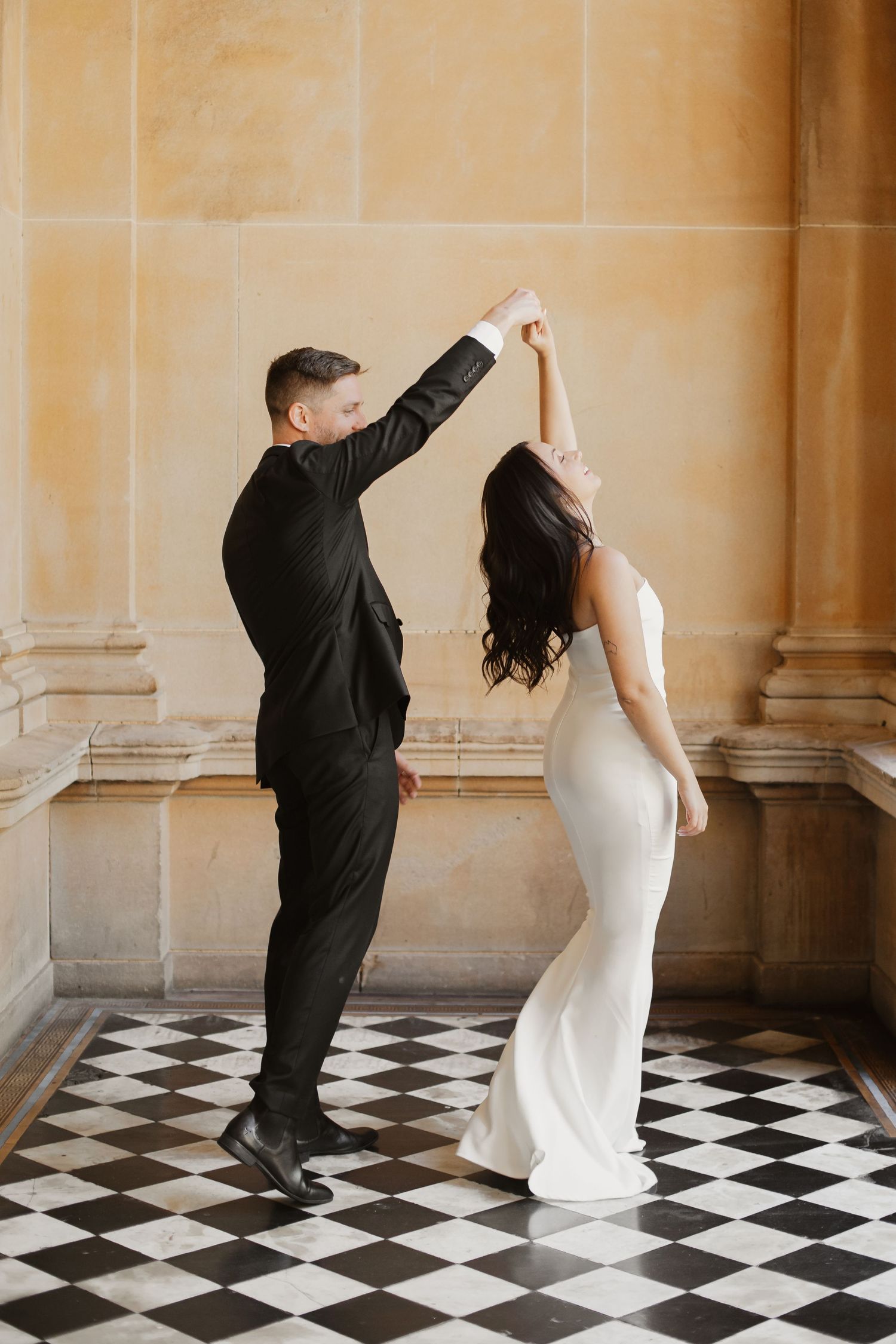 Wedding dance pose on checkered floor with classical architectural backdrop.