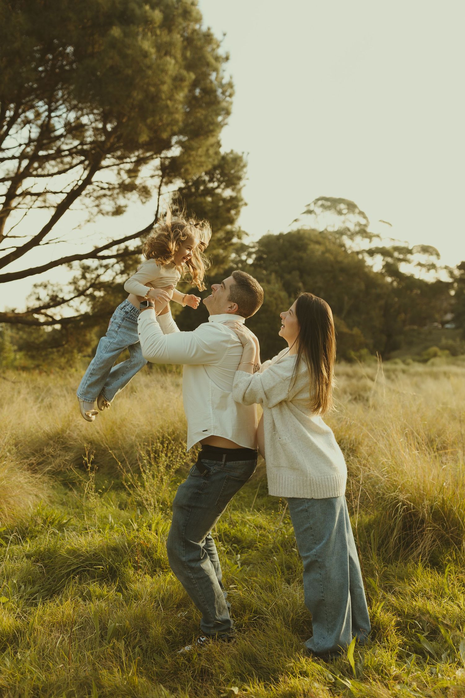 Two people share a playful dance moment in a grassy field during golden hour.