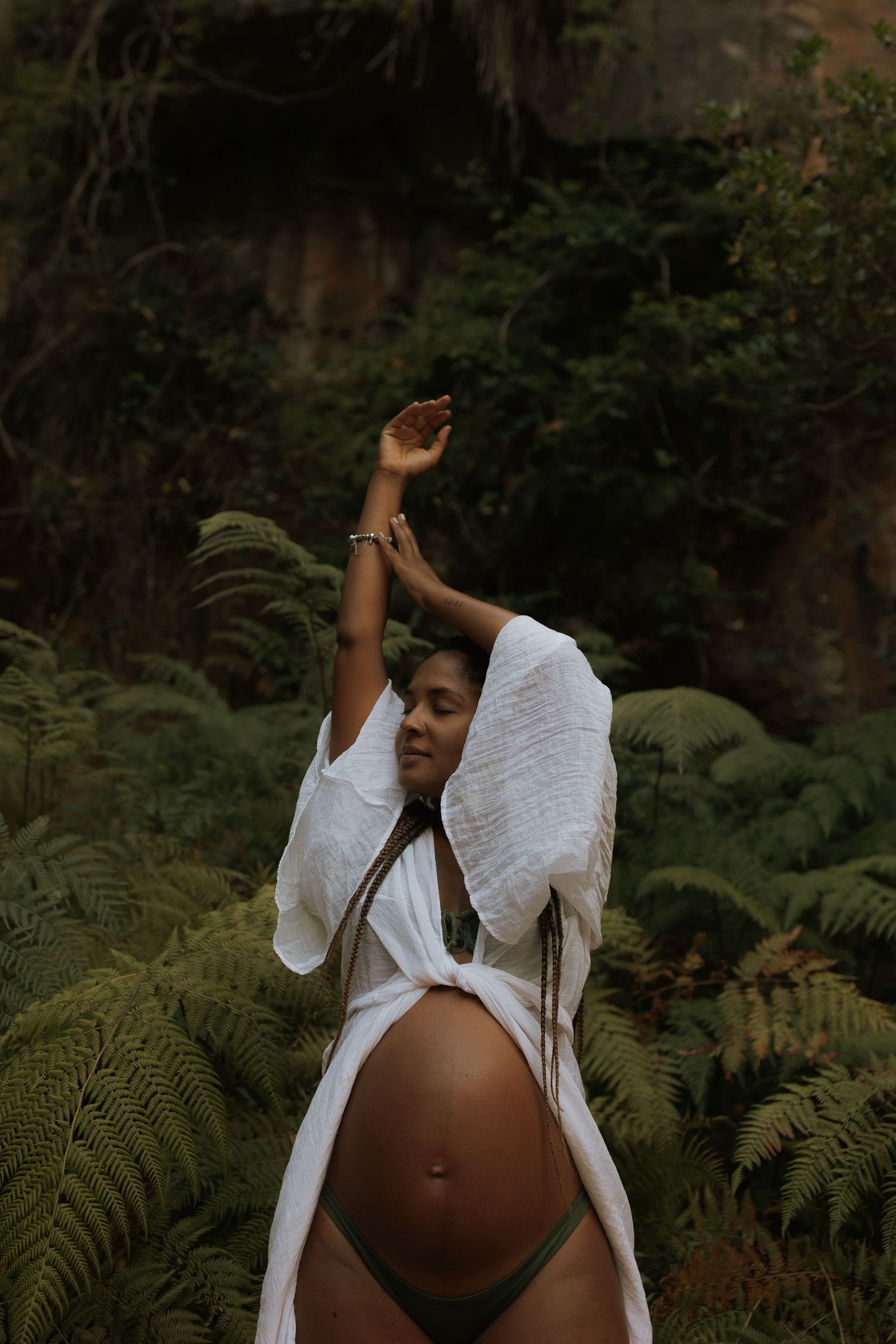 A maternity photo shoot in a lush garden setting with ferns and natural greenery.