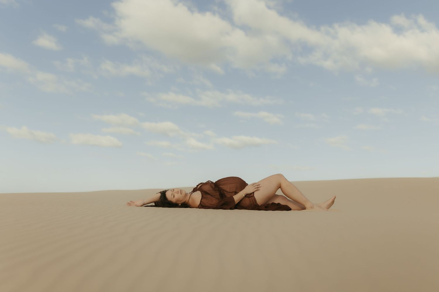 A panoramic view of vast rolling sand dunes stretching to the horizon under a cloudy desert sky.