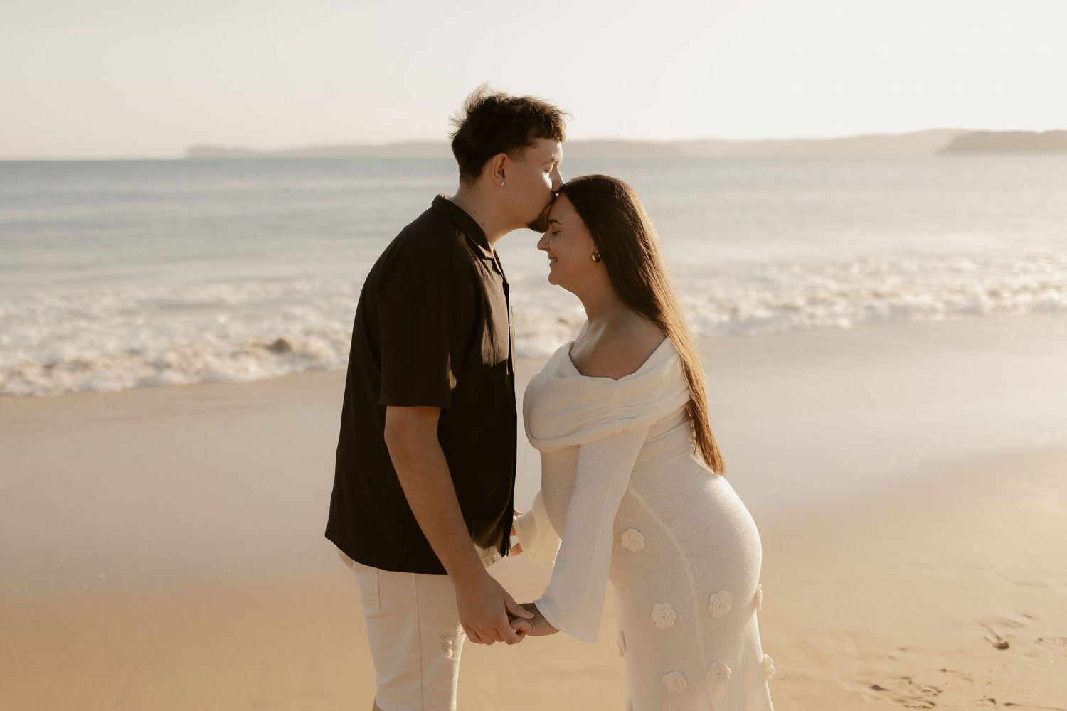 A romantic couple sharing an intimate moment on a beach during golden hour.