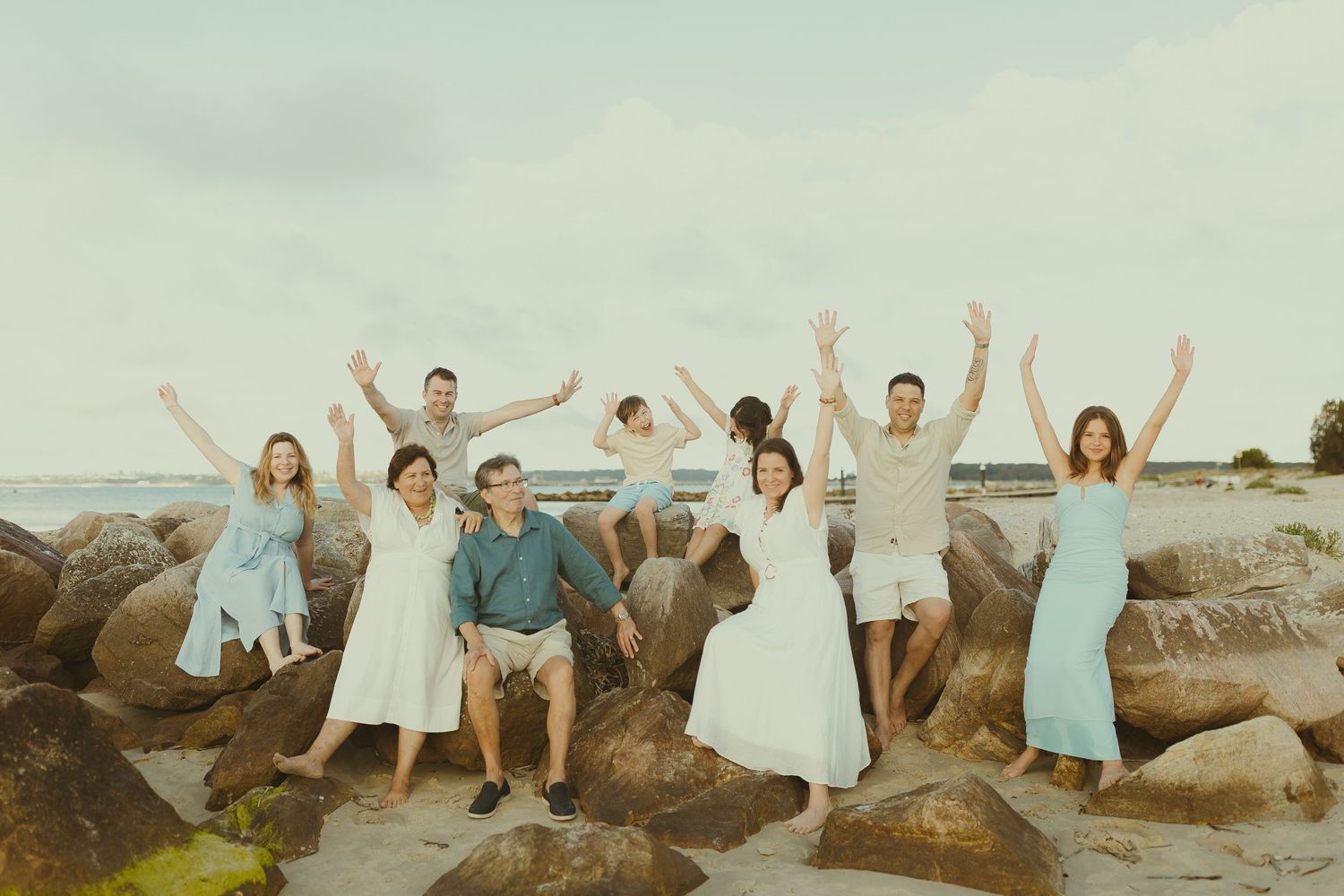 A sequence of photos showing a group of people in white clothing posing joyfully on coastal rocks at sunset.