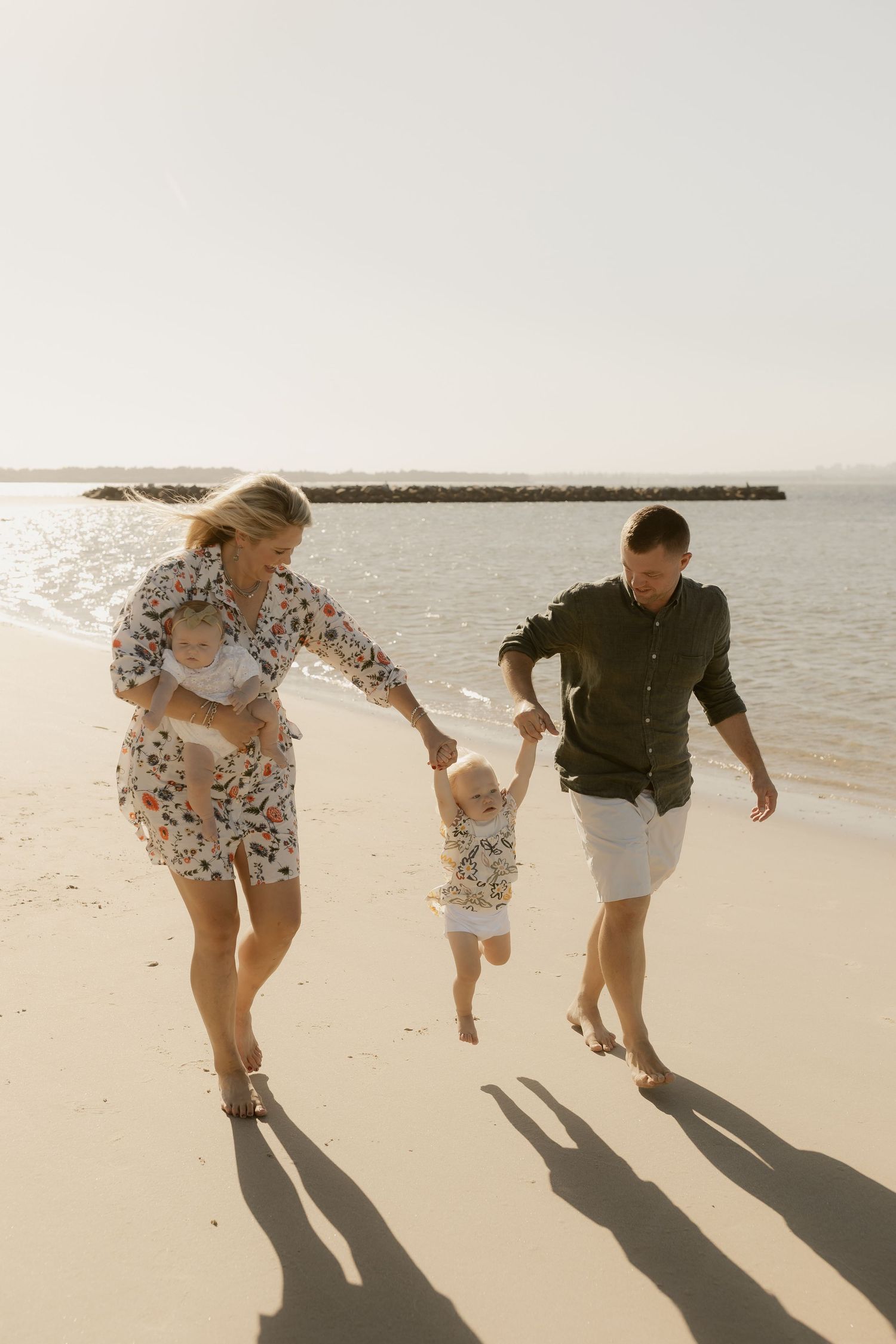 Family walking and playing together on a sandy beach with long shadows cast by the setting sun.