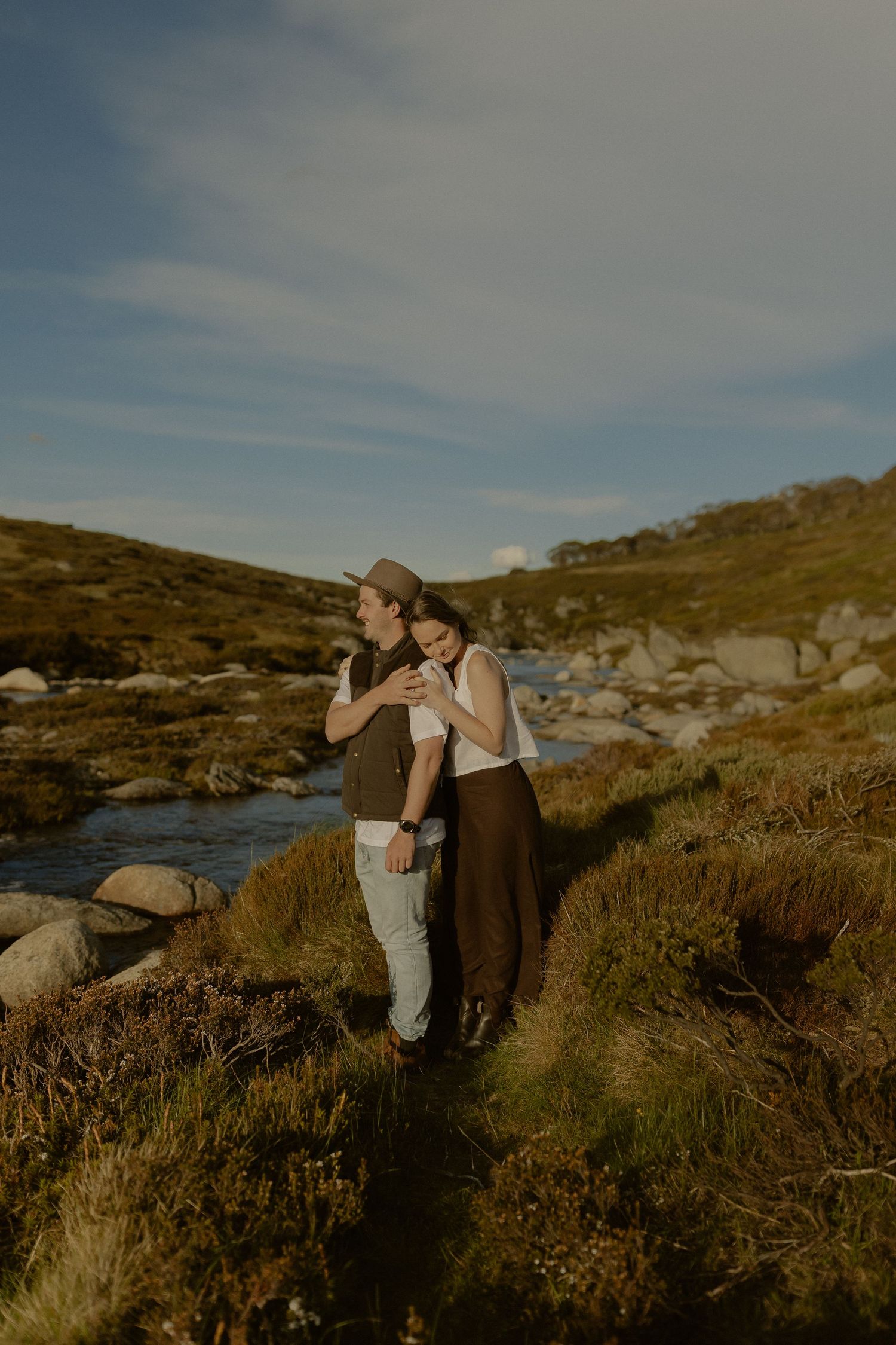 A couple shares an intimate moment against a rocky coastal landscape during golden hour.