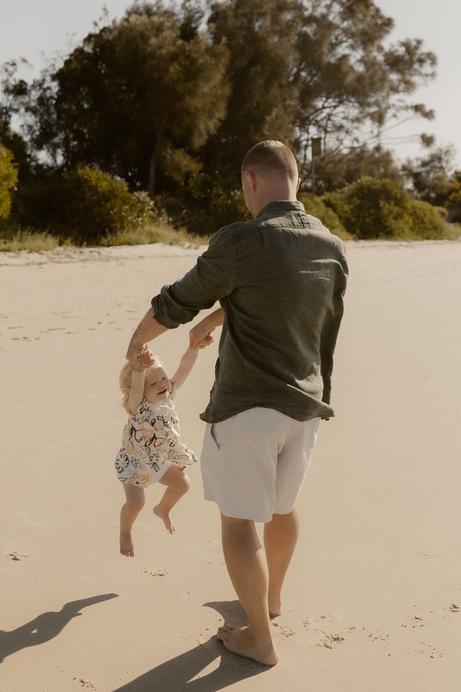 Two people running and playing together on sandy dunes at a beach on a sunny day.