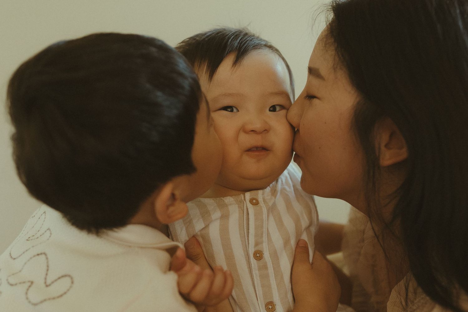 An intimate family moment showing tender affection with a baby in a striped outfit.