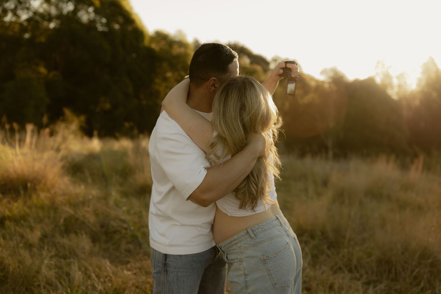 Couple embracing in golden sunset field, man kissing woman's head outdoors.
