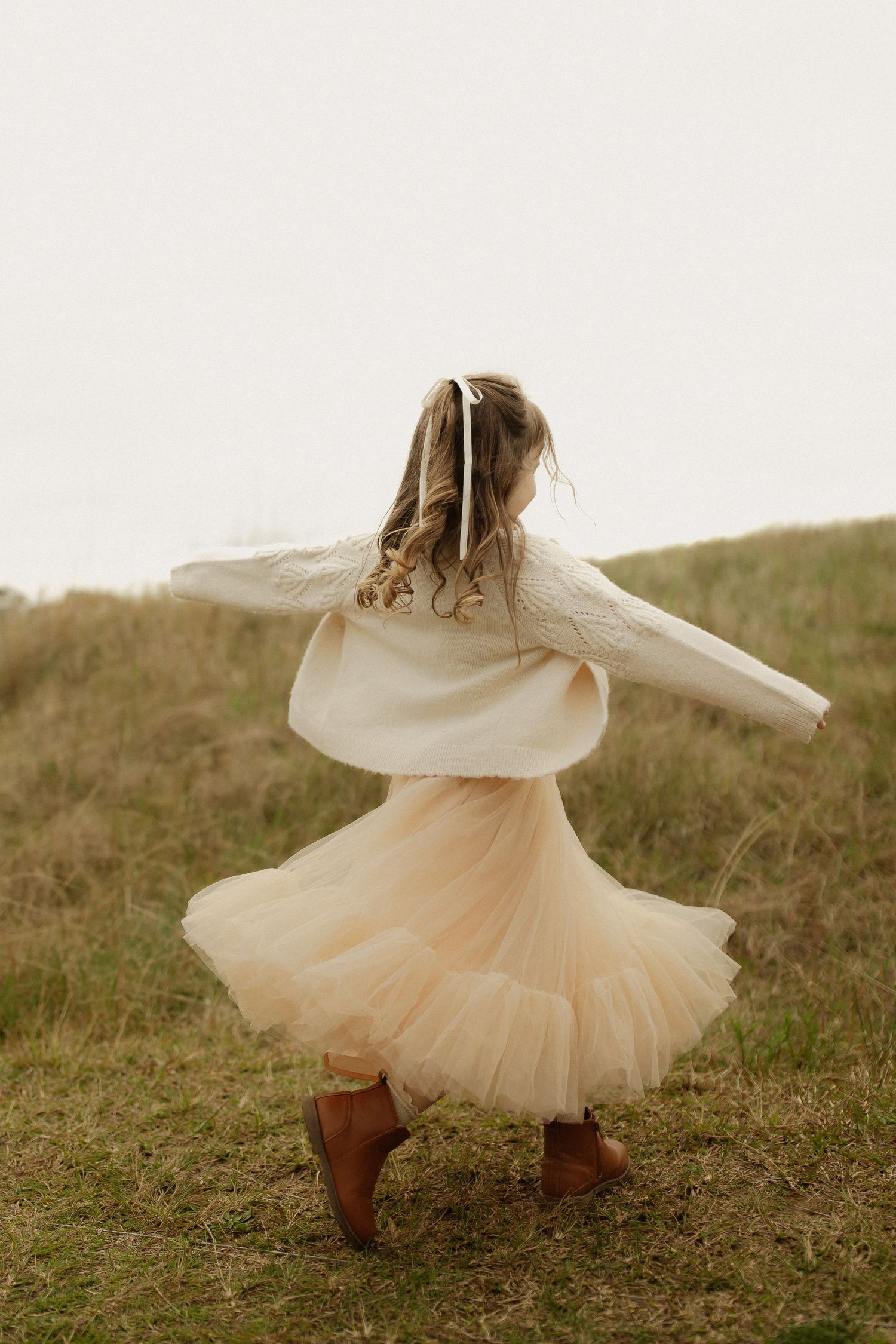 A flowing white tulle dress twirls against a natural outdoor backdrop.