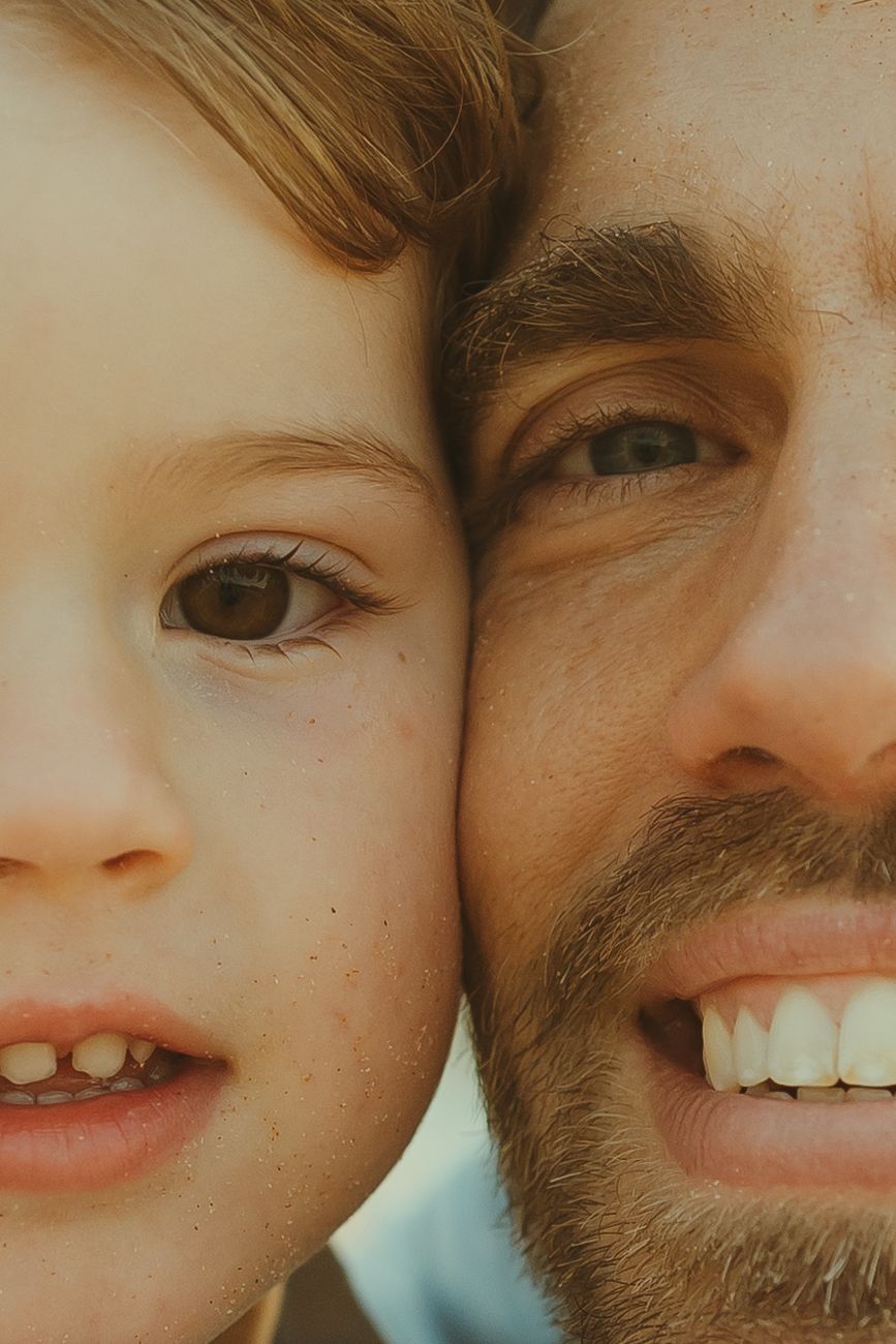 Close-up portrait of two smiling faces side by side showing bright teeth and warm expressions.