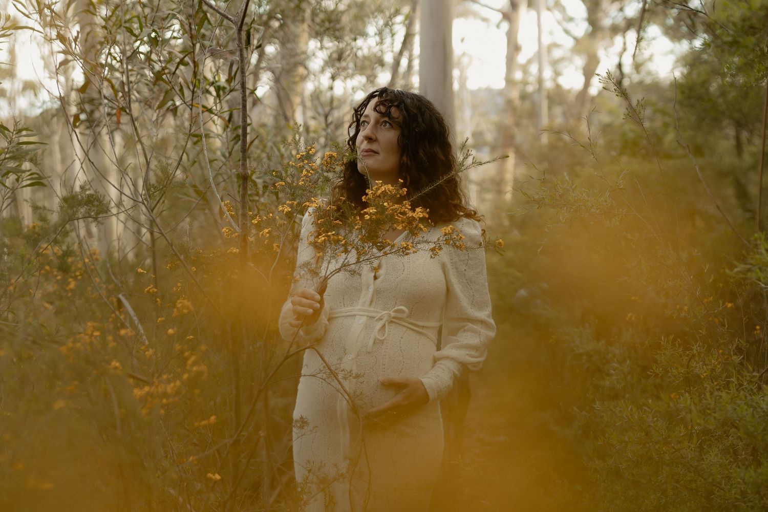 A person in a light colored sweater stands in a misty autumn forest during golden hour.