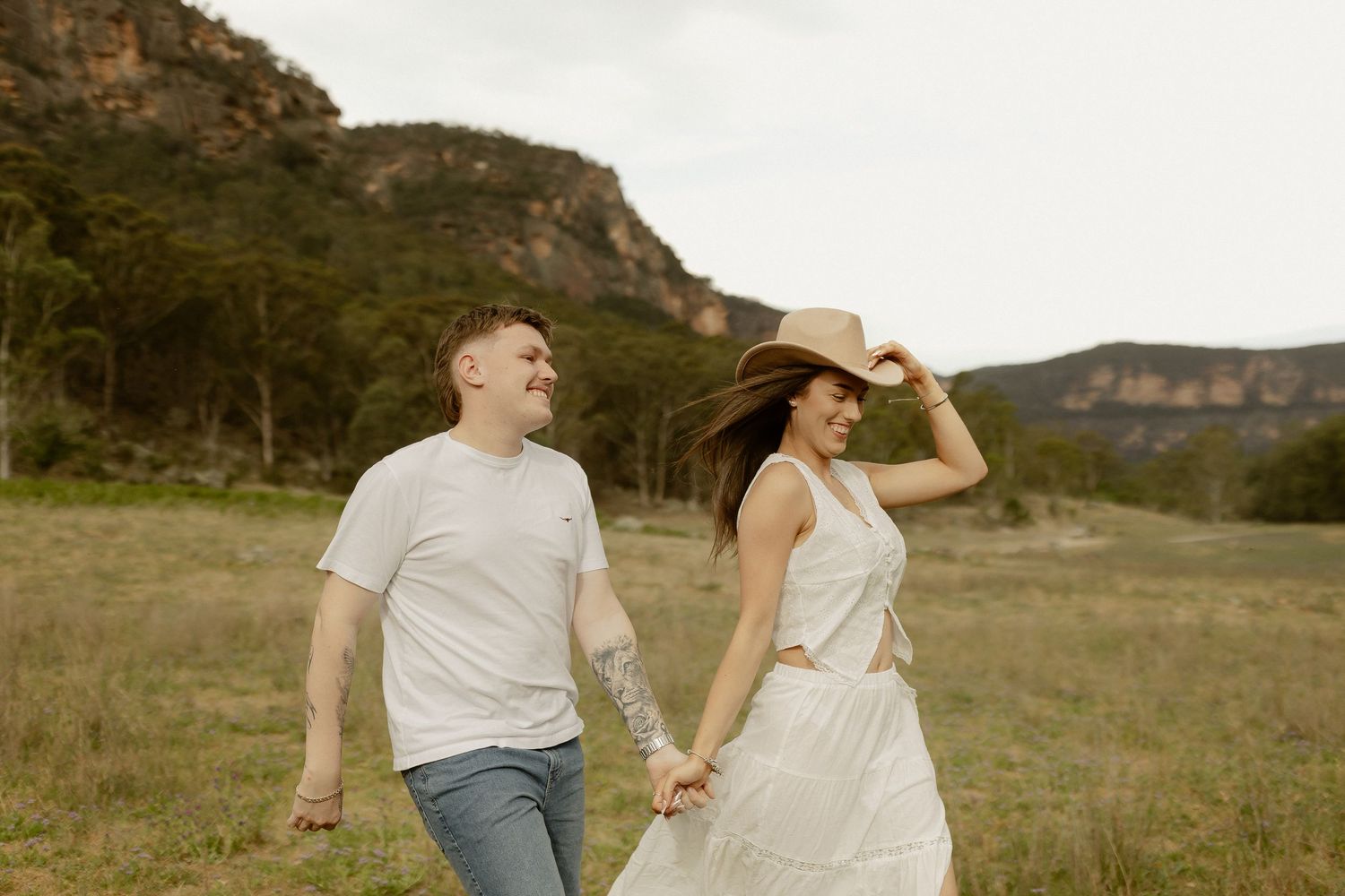 A couple in casual attire walks together through a scenic golden field at sunset.