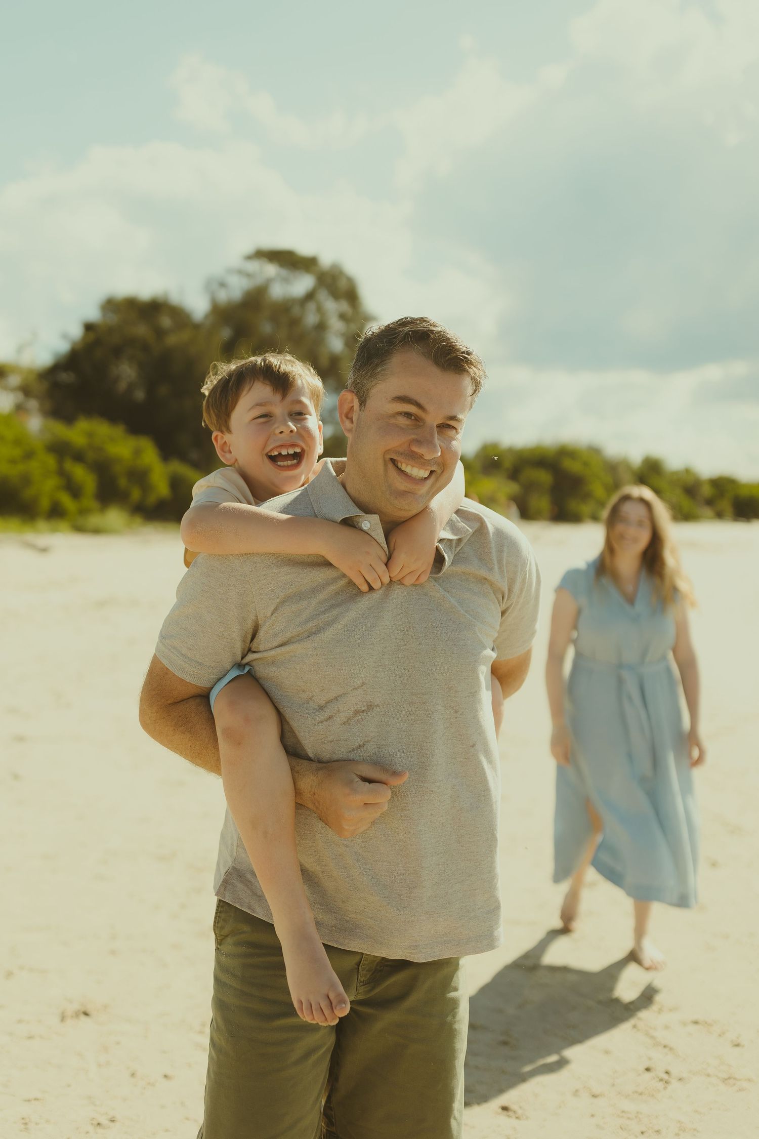 A joyful scene of family members laughing and playing together on a bright sandy beach.
