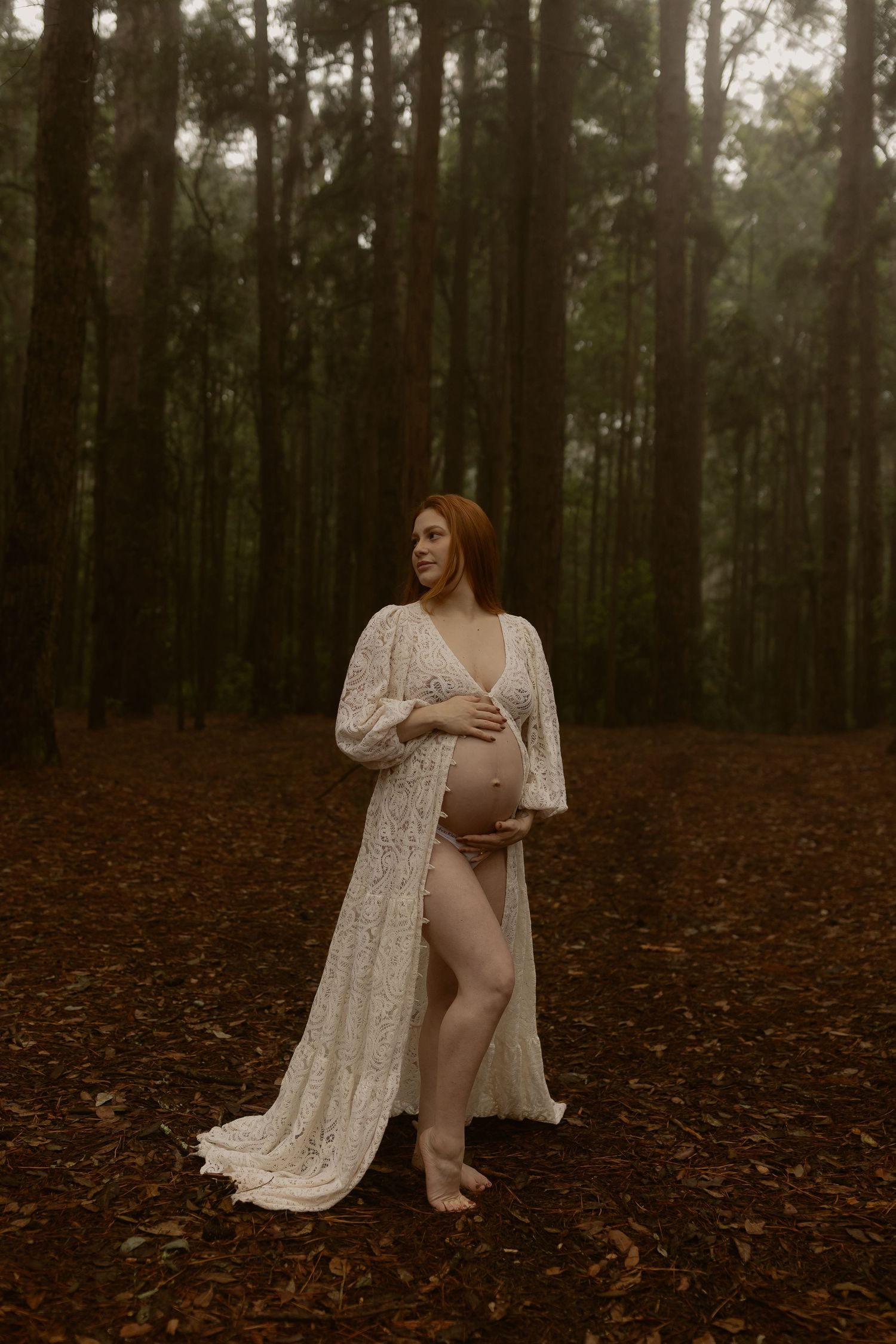 Ethereal figure in white lace dress poses gracefully on forest floor covered in autumn leaves.