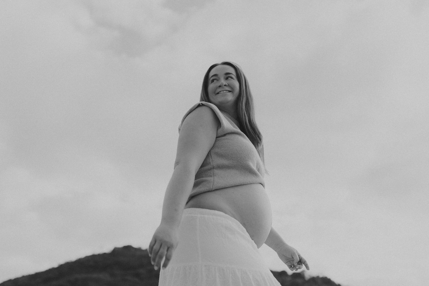 Low angle black and white portrait shots of a person posing against a cloudy sky.