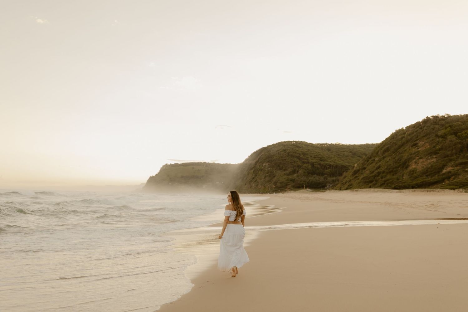 A dreamy beach wedding scene with soft sunlight illuminating the sandy shore and ocean waves at sunset.