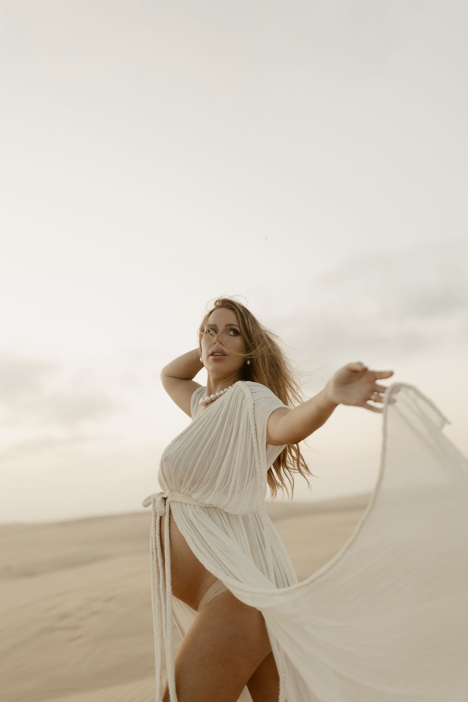 A figure in a flowing white dress poses gracefully against a desert landscape at sunset.