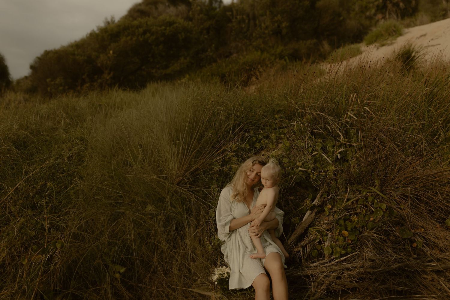 A couple shares a romantic moment on a grassy hillside at sunset with soft golden light illuminating the scene.