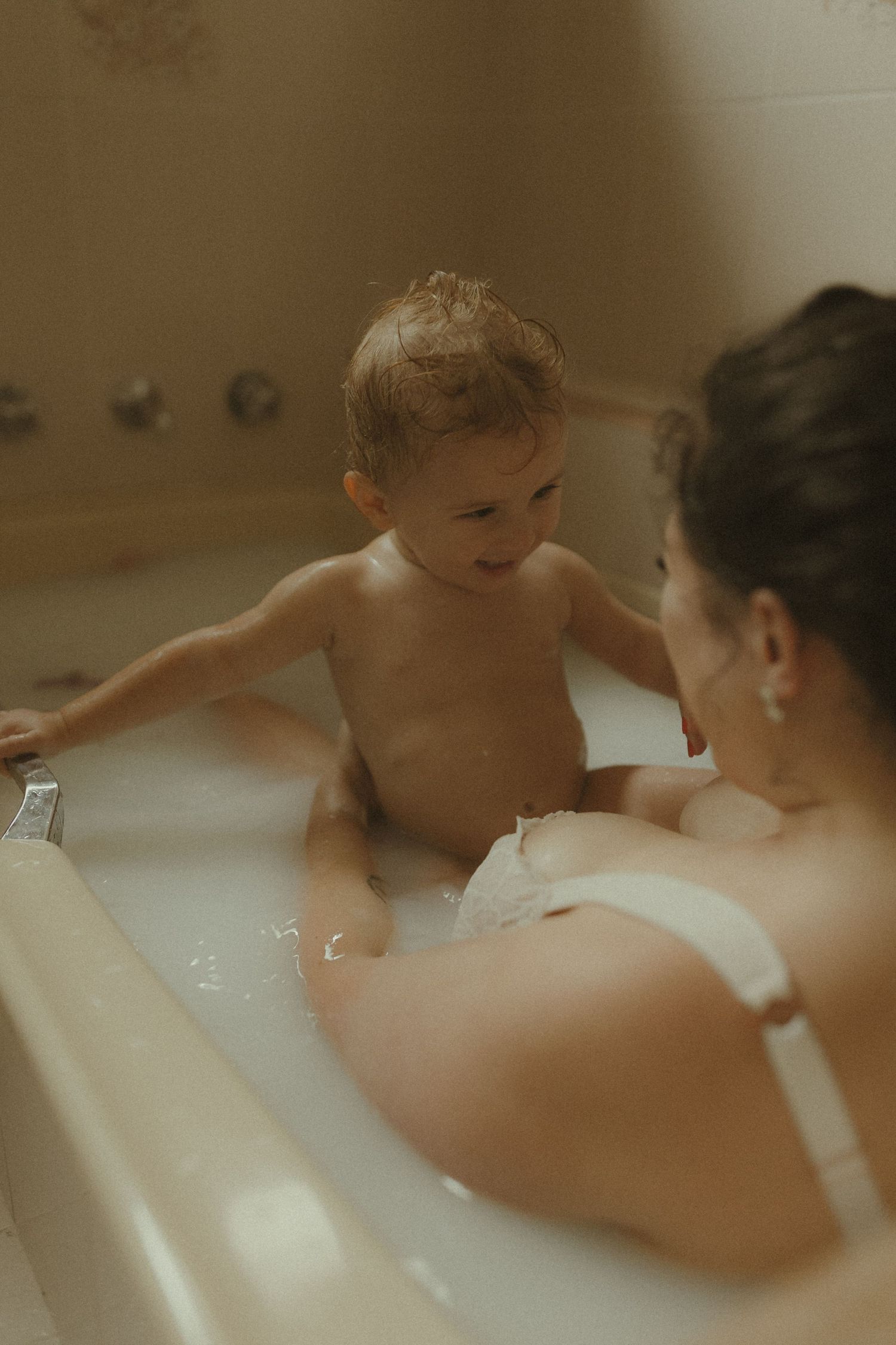 An intimate bath time scene with gentle interaction between caregiver and small child in a bathtub.