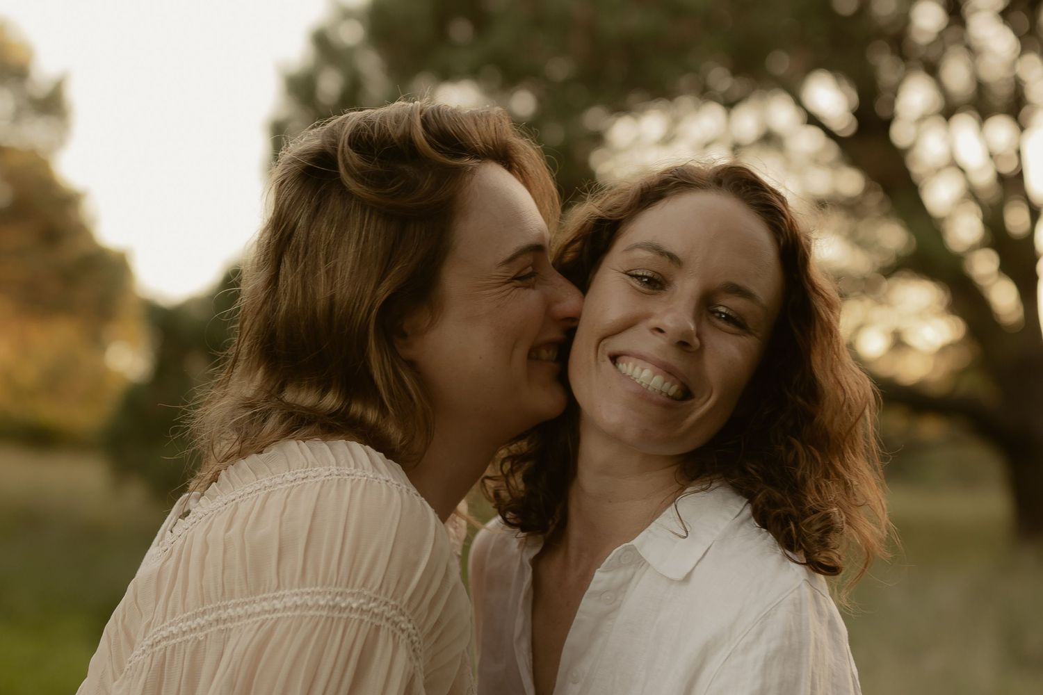 A couple embraces and laughs together in a sunlit outdoor setting during golden hour.