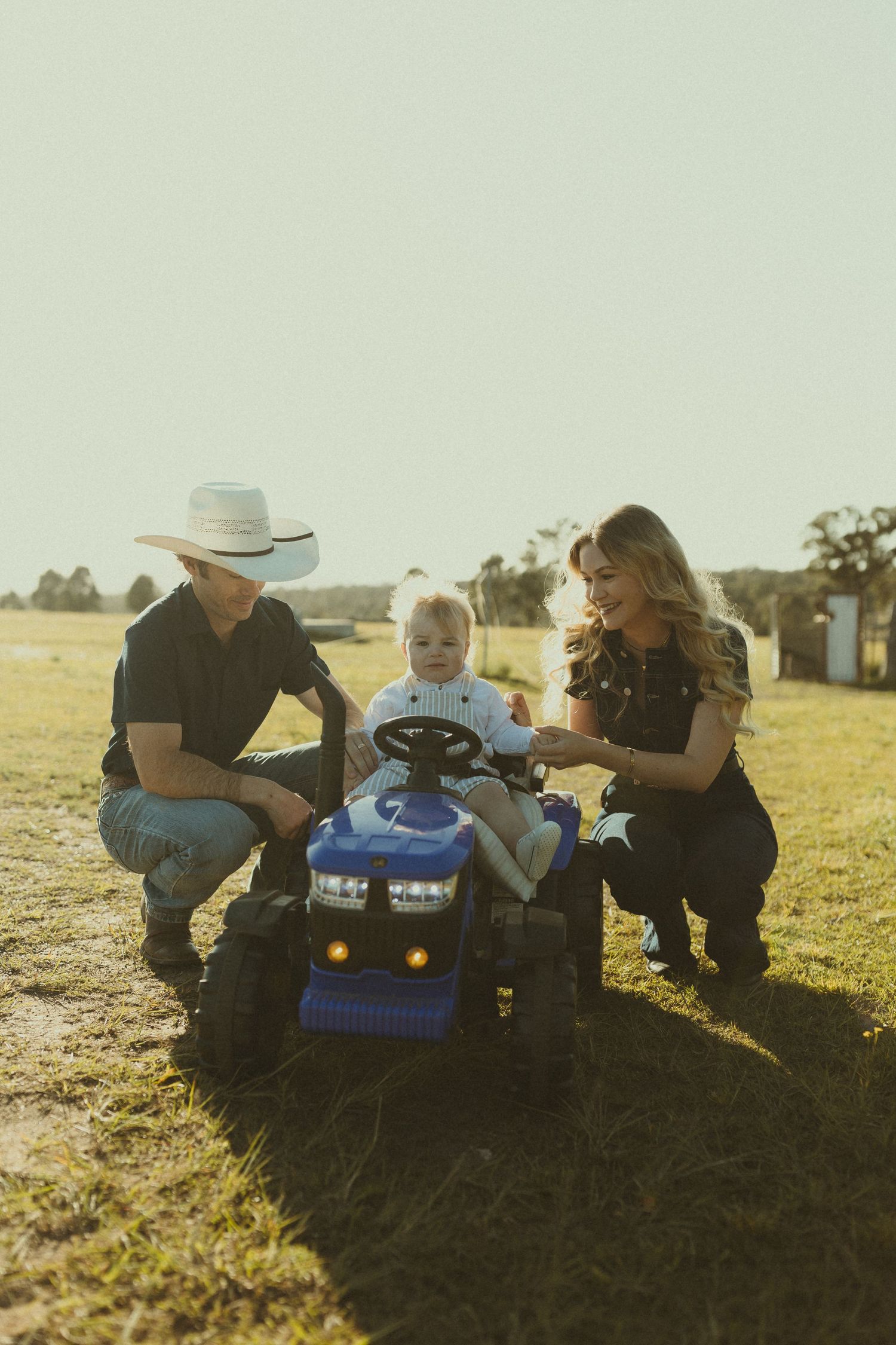 Family playing with a small blue toy car in a sunlit field during golden hour.