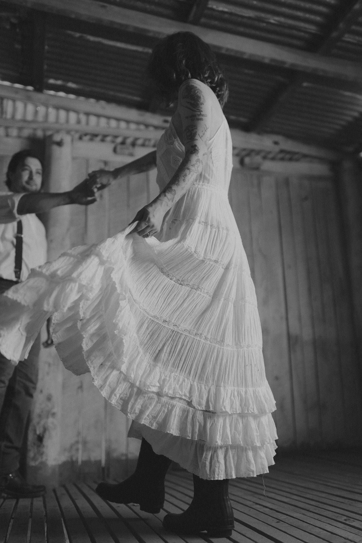 Dancing figure in flowing white dress twirls inside rustic barn setting.