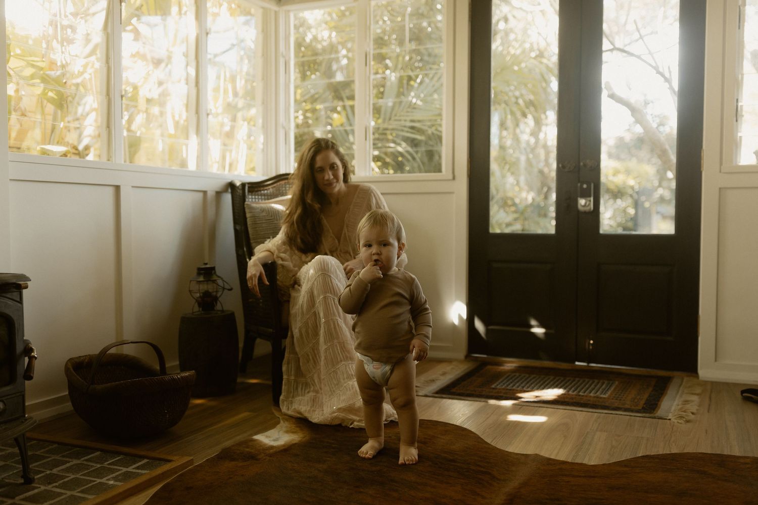 Sunlit moment captured in home interior with baby and adult in white dress.