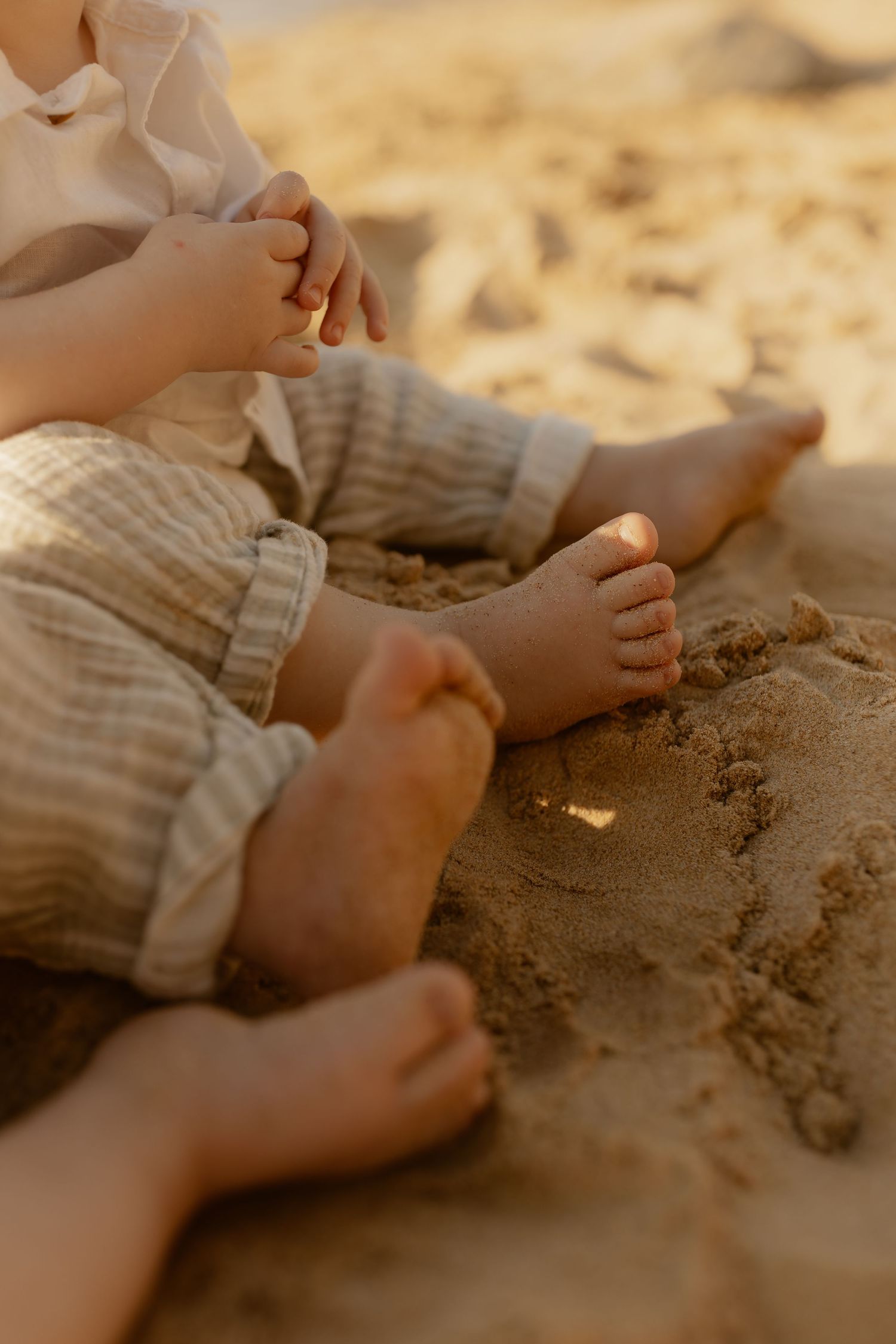 Close-up shots of tiny feet playing in golden beach sand during sunset.