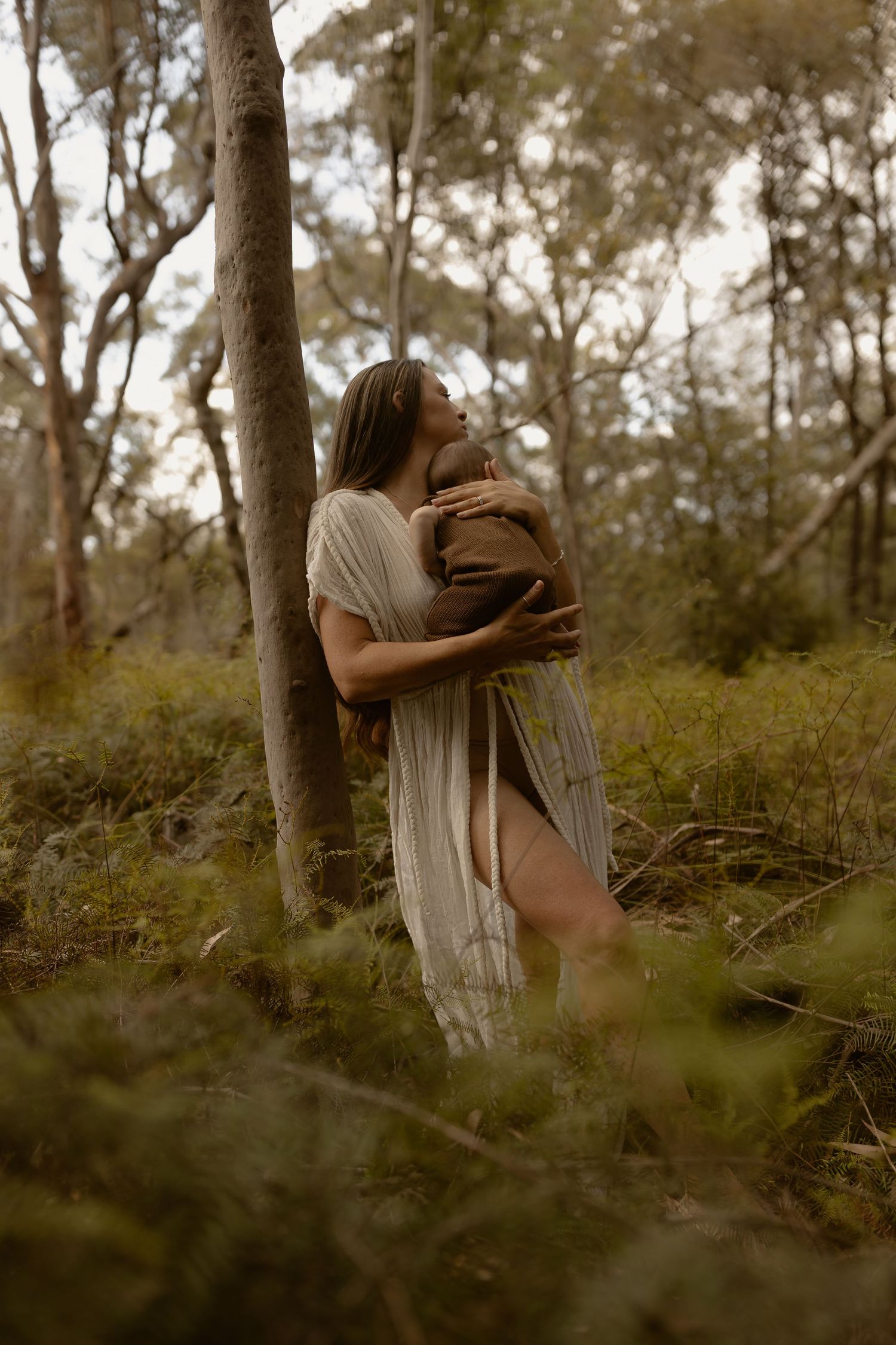 A couple in white dresses embraces tenderly among trees in a dreamy forest setting.