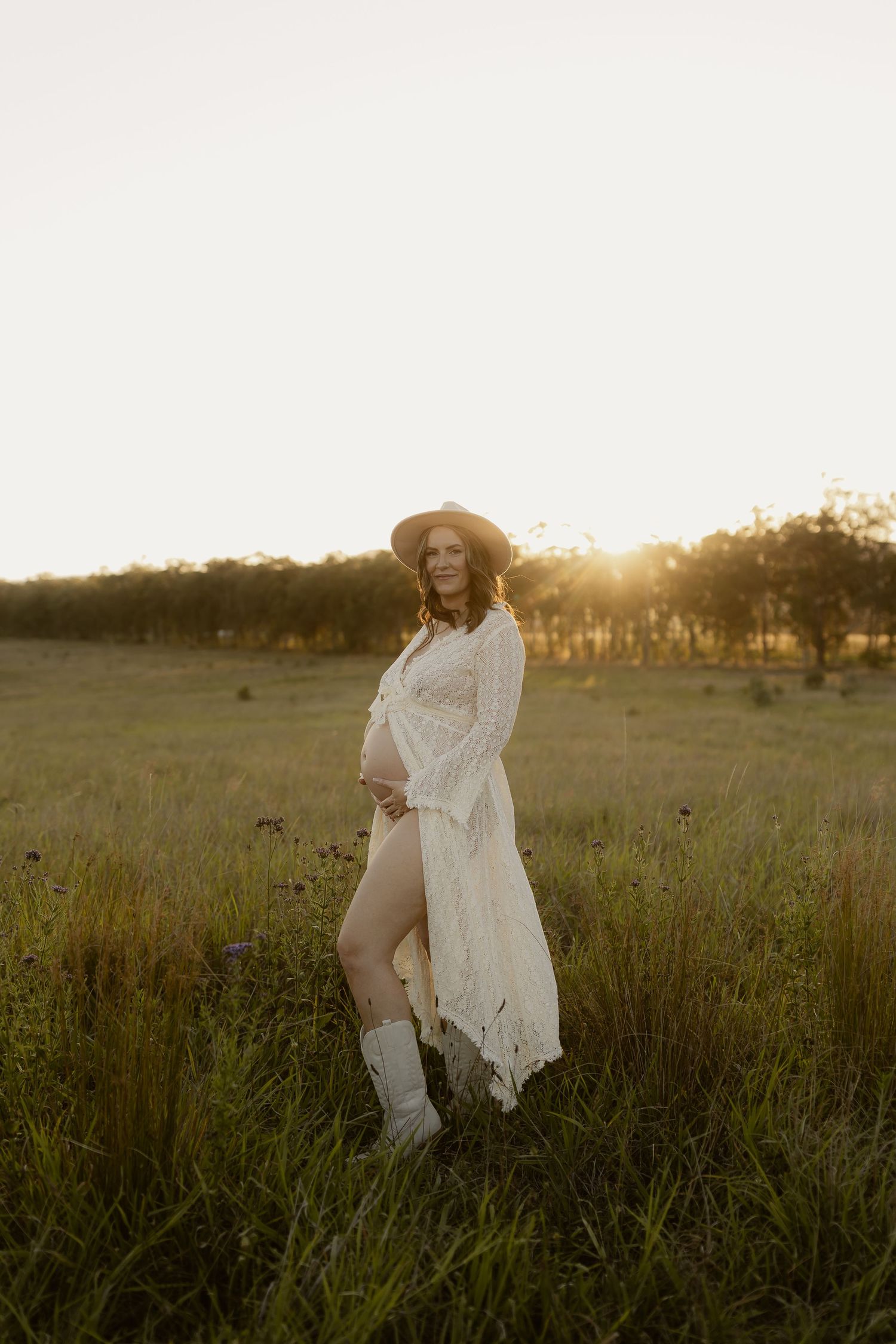 A romantic boho-style portrait in a sunlit field wearing a white lace dress and cowboy boots.