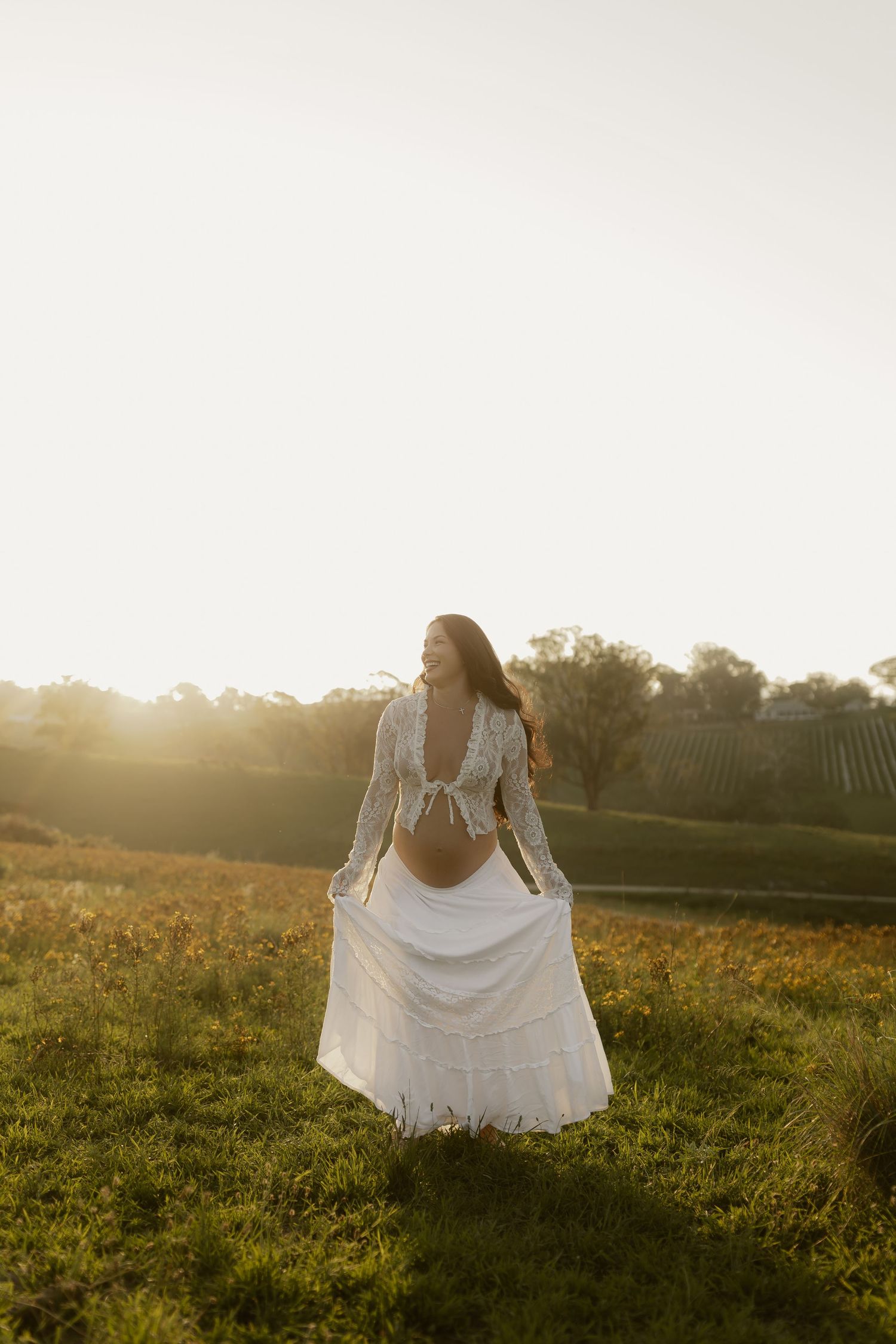 A flowing white dress catches the golden light in a serene meadow setting.