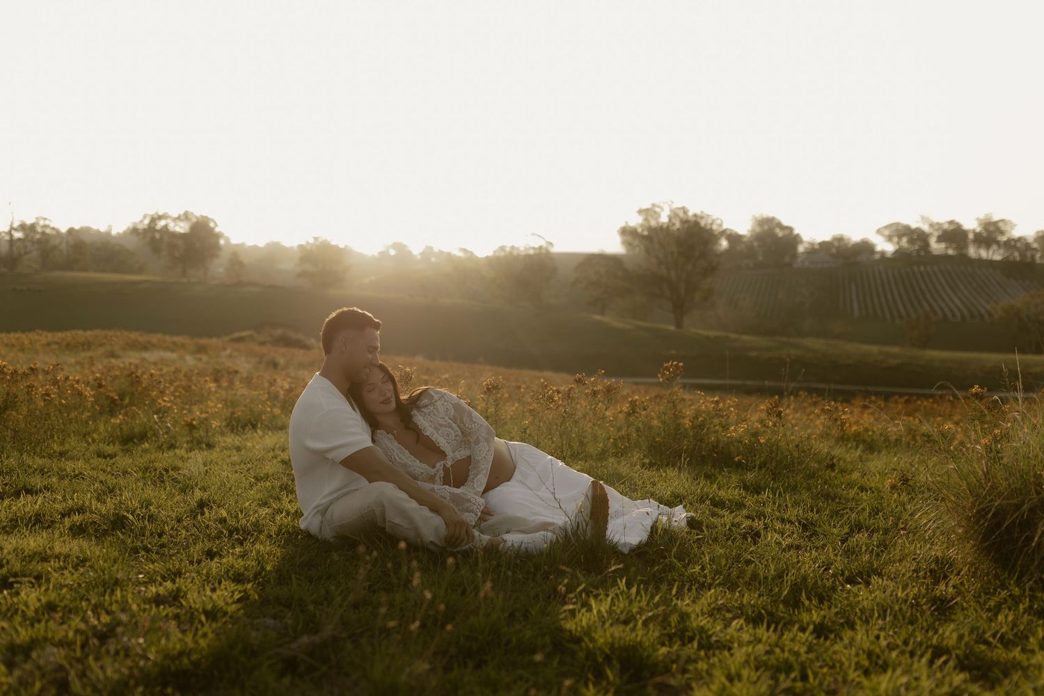 Couple lies together on grass overlooking scenic mountain landscape at sunset.