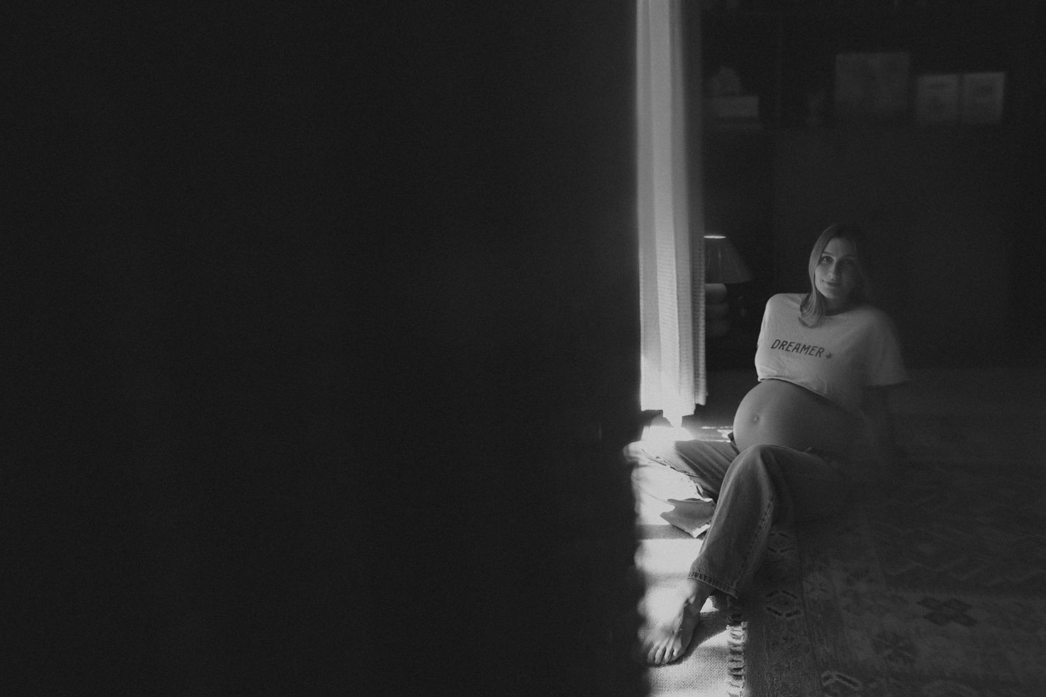Black and white photo of a person sitting on the floor in a dimly lit room, illuminated by a narrow beam of light.
