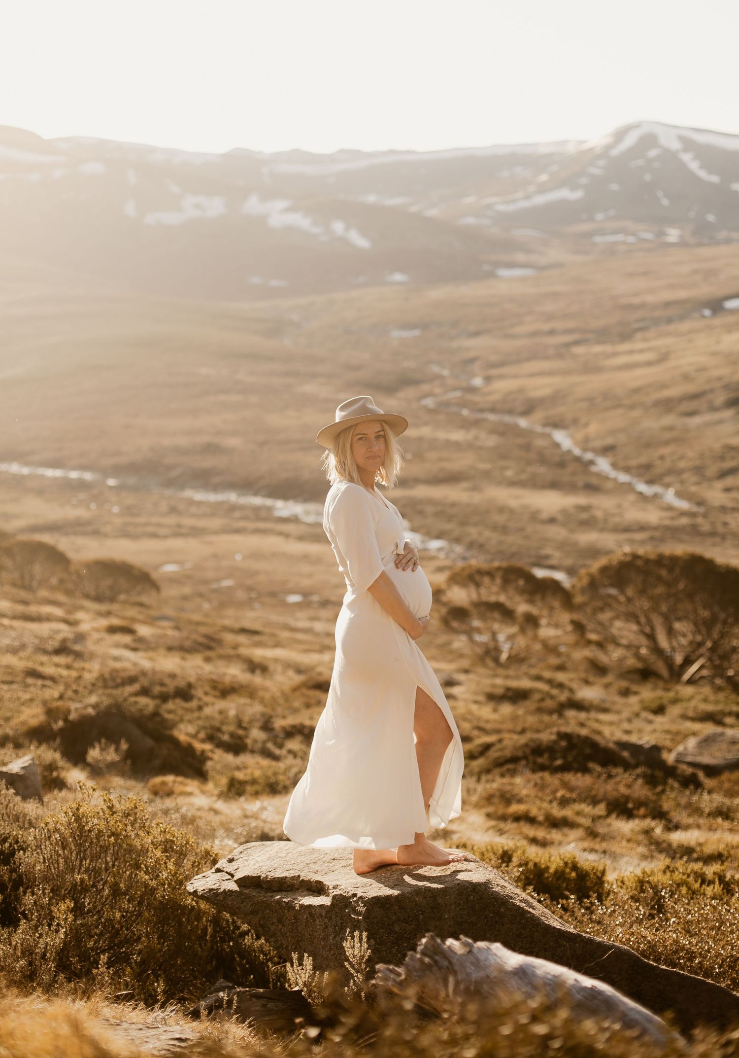 White dress silhouetted against golden mountain landscape at sunset in Australian high country.