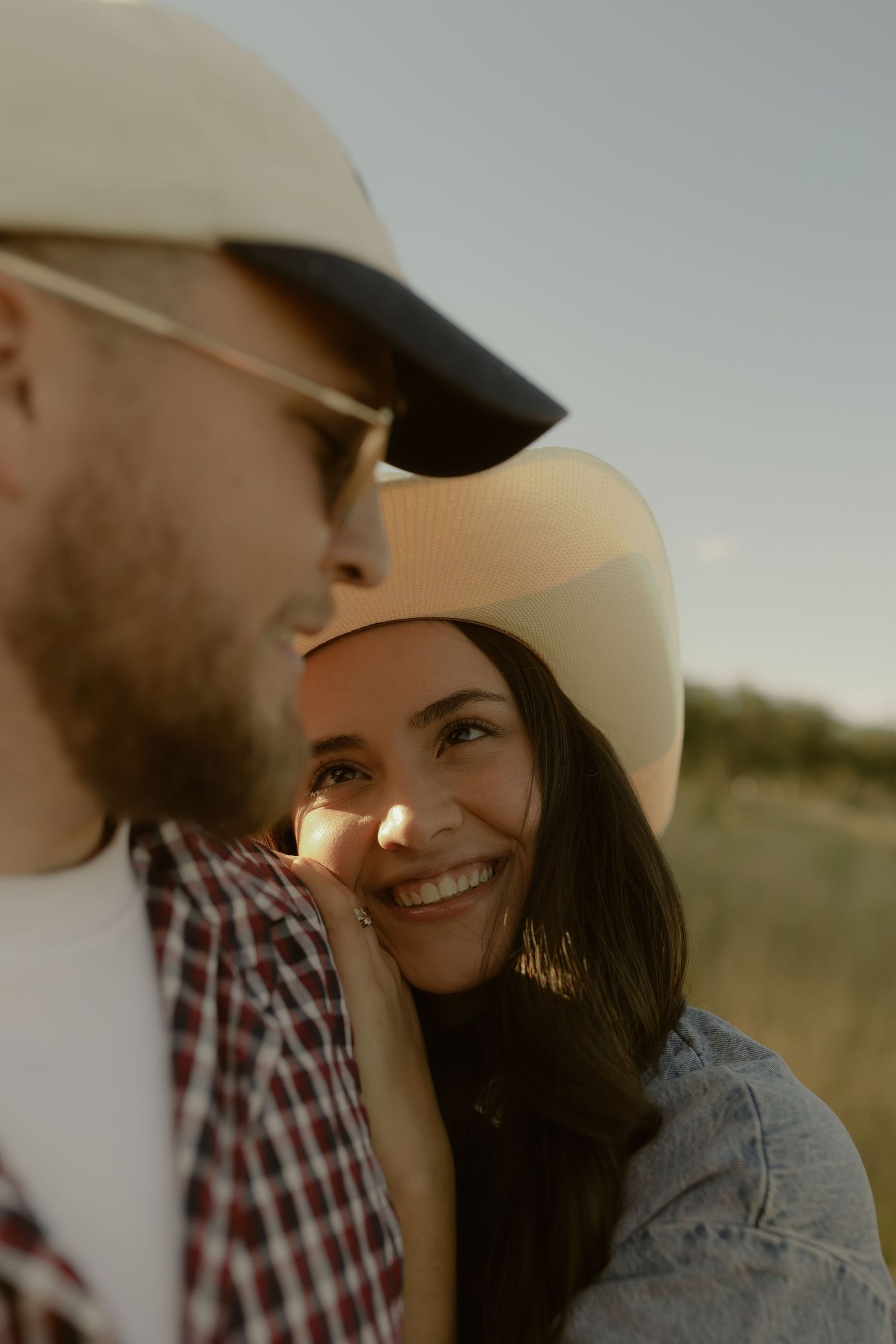 Smiling woman in cowboy hat leans against man outdoors at golden hour.