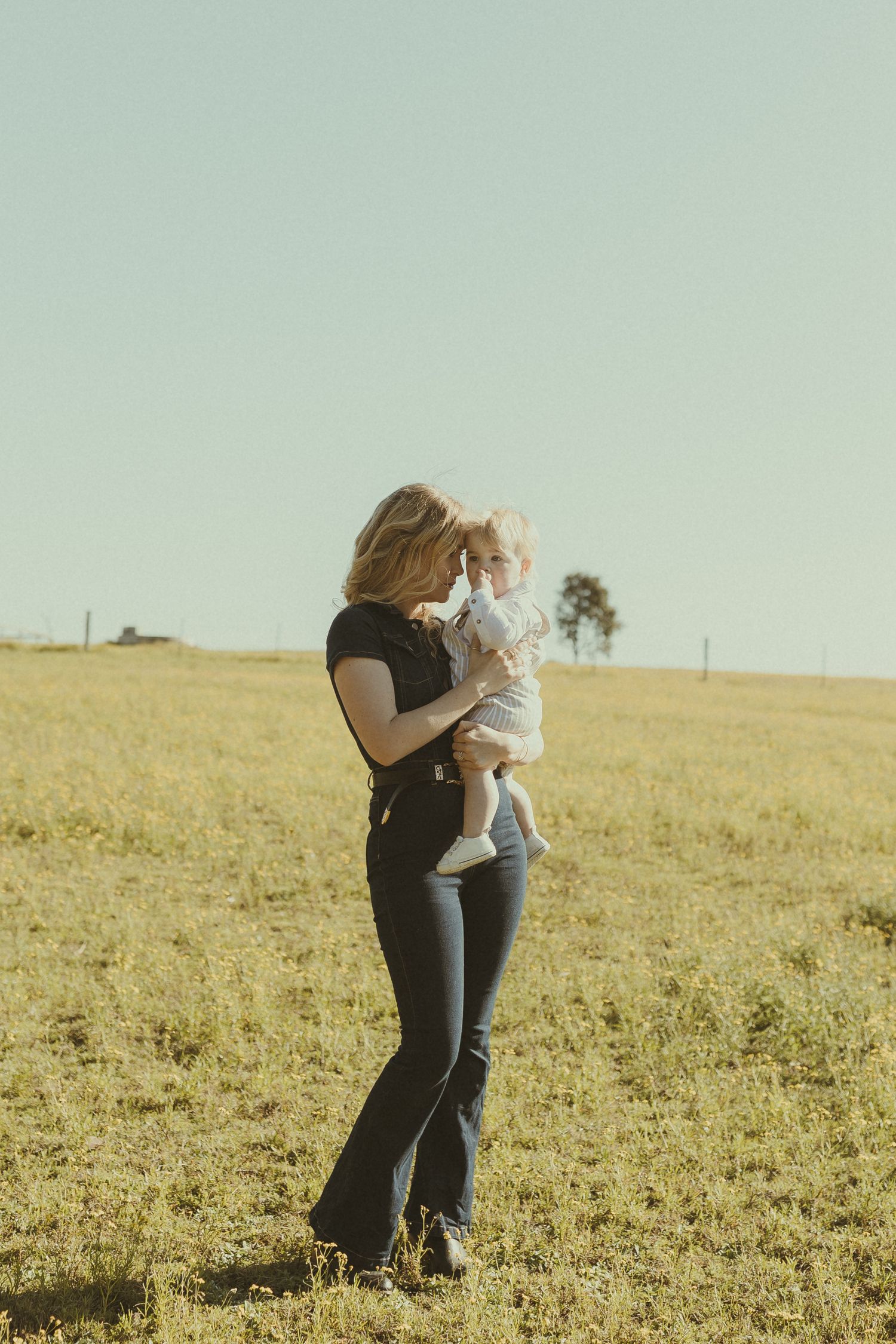 A tender moment between two figures standing in a golden sunlit field on a clear afternoon.