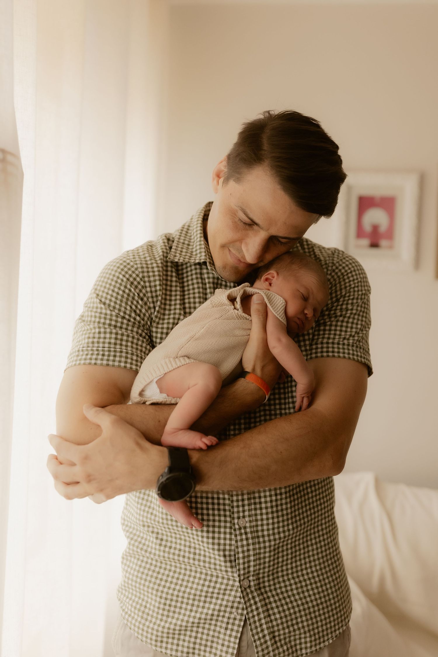 Parent in gingham shirt holding and kissing newborn baby in emotional photo series.